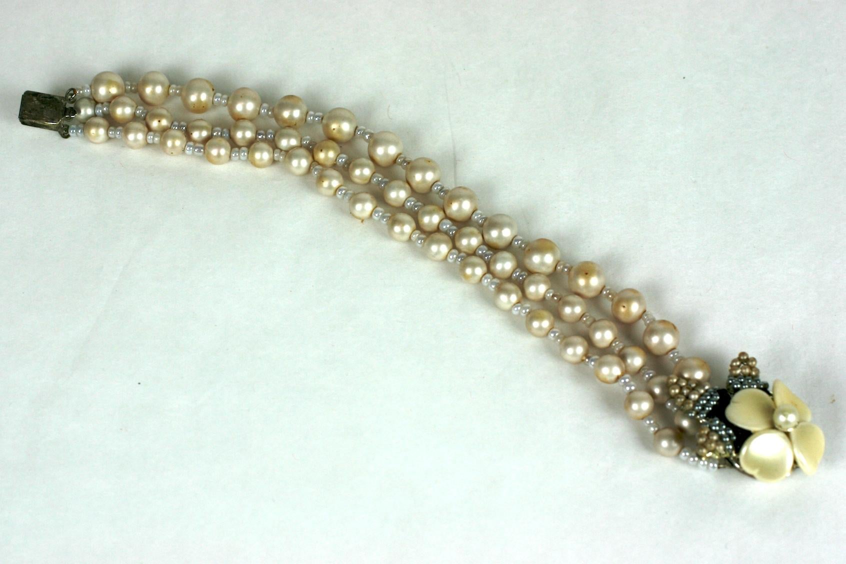 Miriam Haskell freshwater signature faux pearl bracelet. Three strands of round pearls with pearlized seed bead spacers. Elaborate round clasp decorated with a pearl dogwood flower and hand sewn black, grey, and cream smooth and baroque small faux