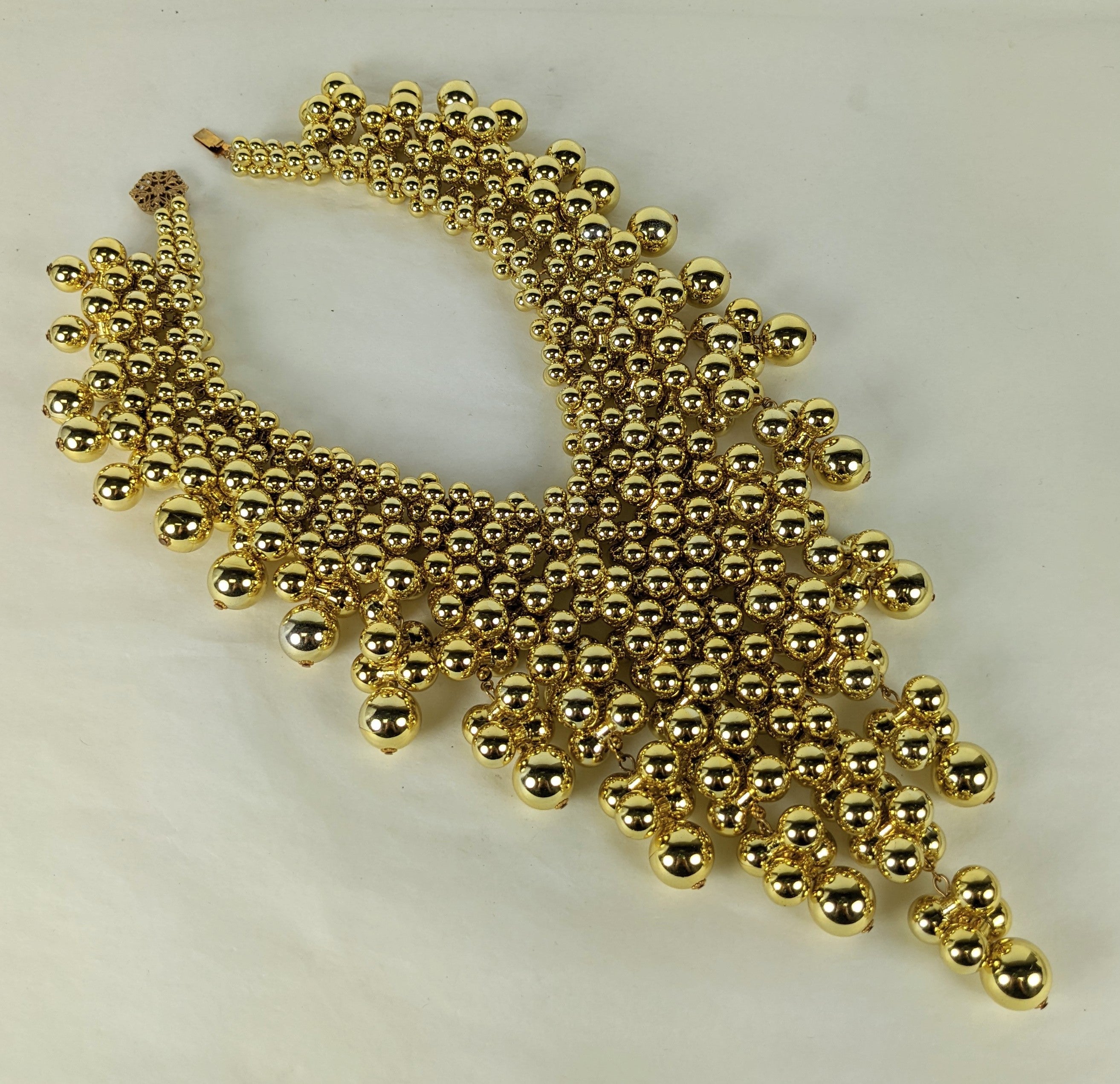Le Gold Bubble Bib de Miriam Haskell est composé de dizaines de cloches muettes en résine plaquée or qui s'imbriquent les unes dans les autres pour former des vrilles de différentes longueurs sur ce collier massif mais léger. 
États-Unis, années