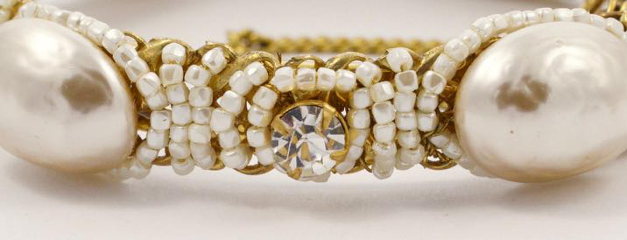 Exquisite Miriam Haskell gold tone bangle, featuring wired large oval baroque pearls, with soft white beads and clear rhinestones. The bangle has a safety chain with the Miriam Haskell hang tag. The bangle is slightly oval, and measures inside