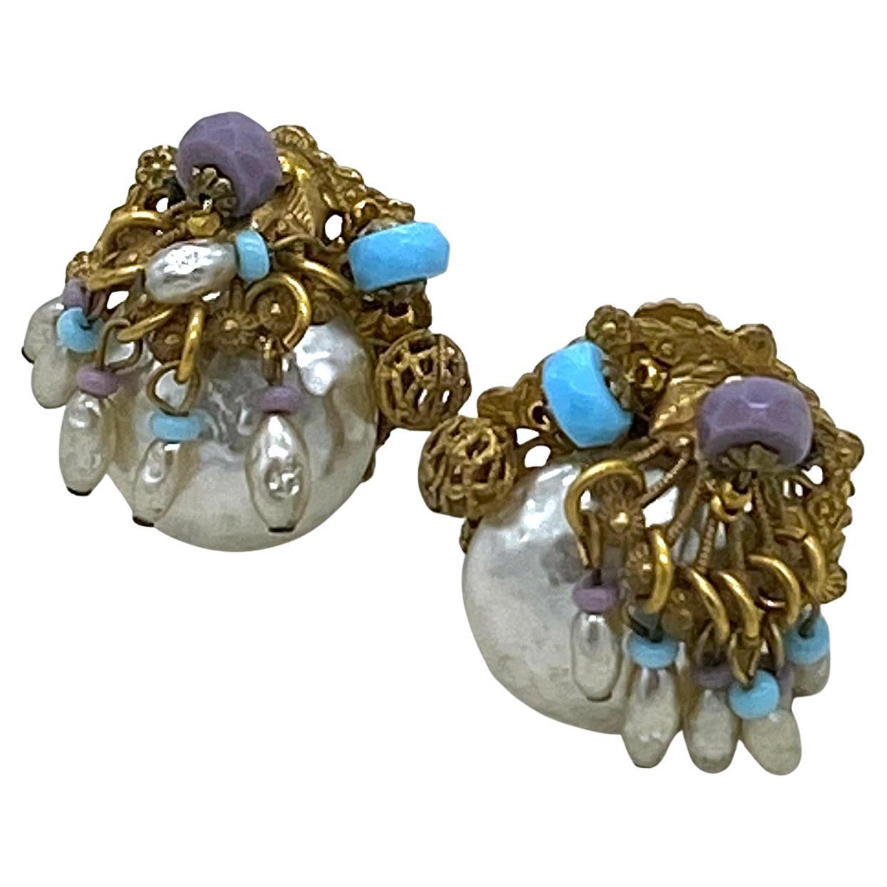 Si tratta di un paio di orecchini Miriam Haskell. Si tratta di grandi perle a bottone e perle blu e lavanda cablate a mano su filigrana d'oro russa. Inoltre, sei maglie di perle di riso penzolano come charme. Firmato Miriam Haskell sul retro