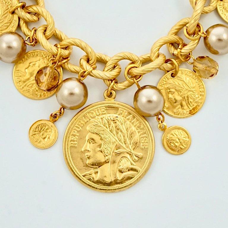 Favoloso bracciale con ciondoli Miriam Haskell placcato oro russo, con perle finte in oro pallido e vetro citrino sfaccettato, e monete decorative greche e francesi. Misura 20,3 cm di lunghezza e la moneta più grande ha un diametro di 2,9 cm. Il