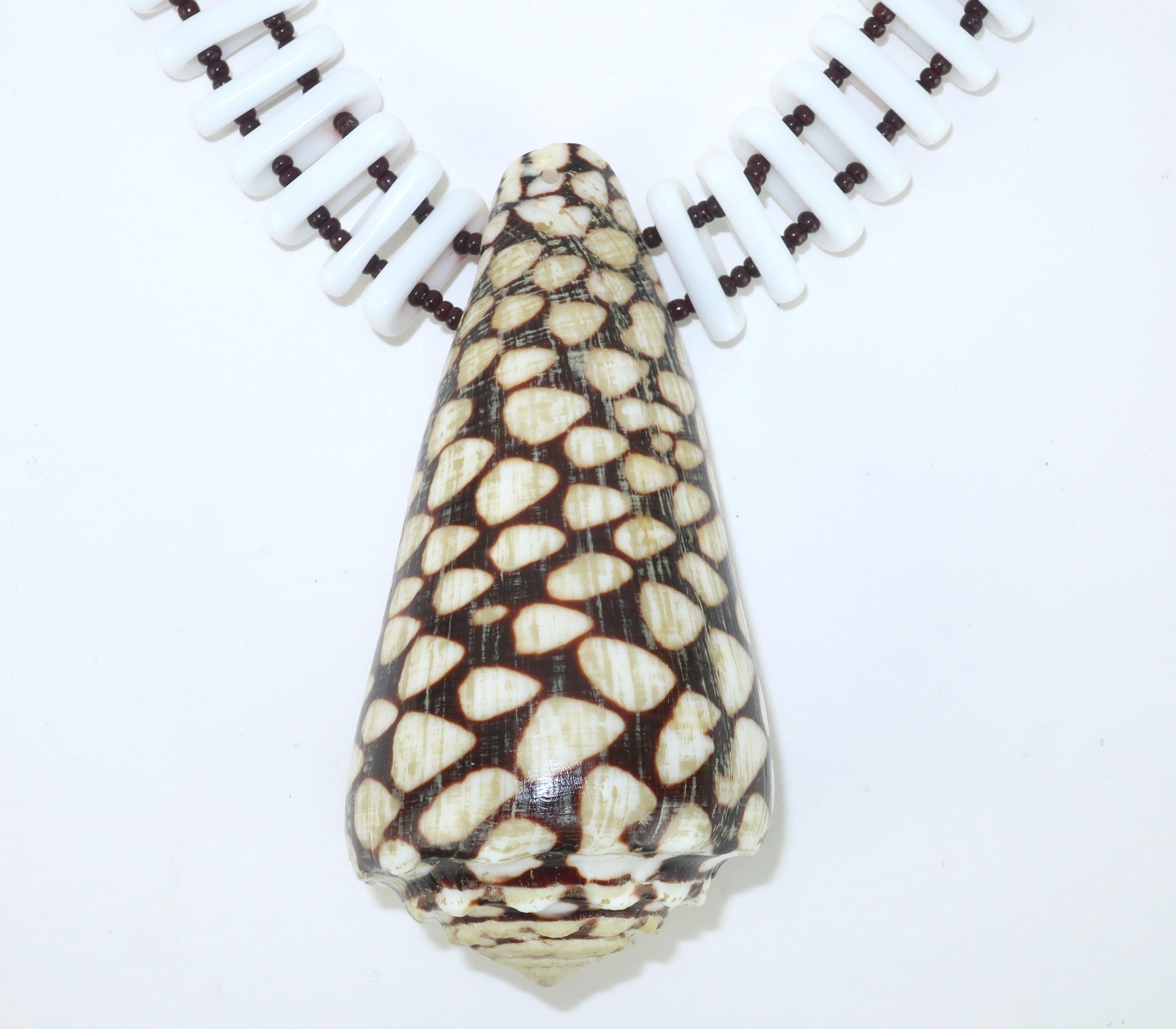 Dramatique dans sa simplicité, ce collier du milieu du siècle de Miriam Haskell combine un pendentif en forme de cône de coquillage tacheté avec des perles de verre blanc en forme de capsule, espacées de perles plus petites de couleur brun foncé