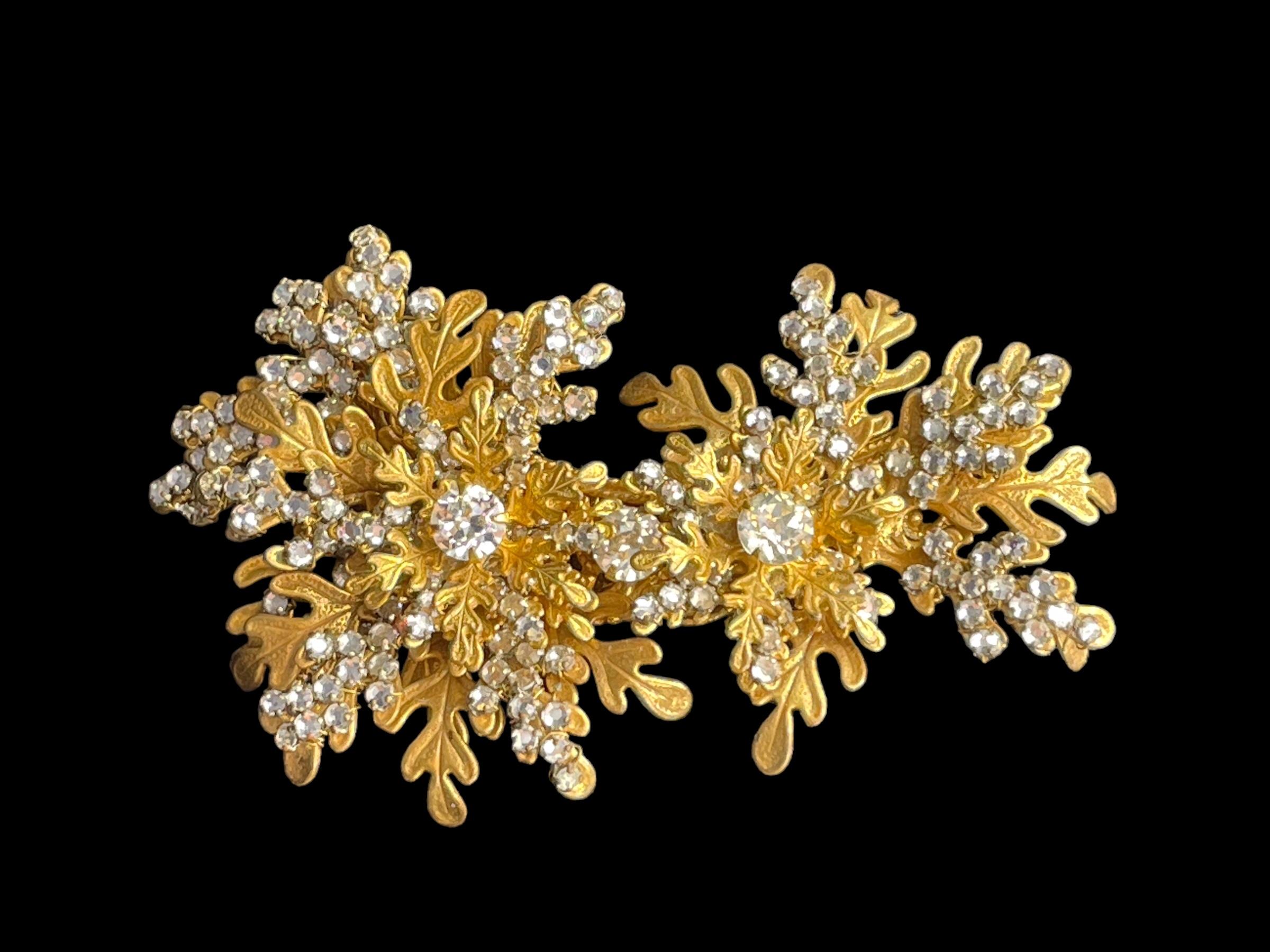 1950s Haskell trembler brooch.
Gilt metal filigree oak leaves are interspersed with clusters of rhinestone berries and highlighted by three larger stones. The two large stones layered at the top of the brooch are set with a wreath of oak leaves.