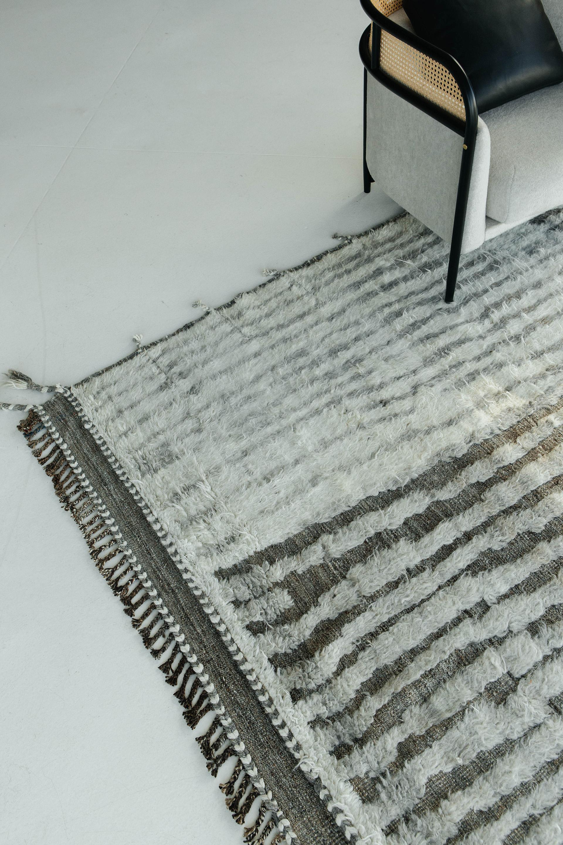 A grey handwoven base flat-weave with embossed detailing streams through this white wool shag rug with heather grey line work moving irregularly from top to bottom. Inspired by the Atlas Mountains in Morocco for the modern design world

Rug Number