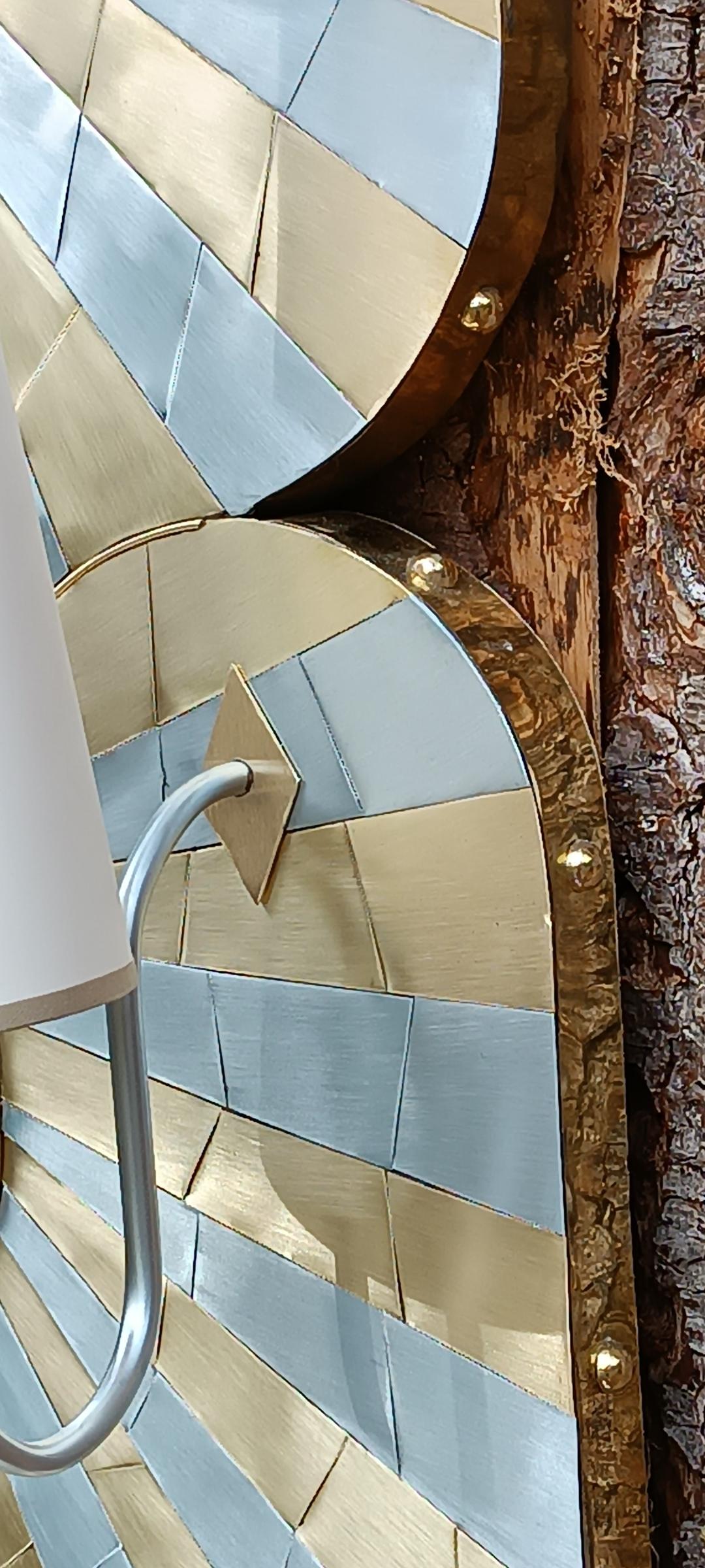 Grand miroir de forme libre et ses appliques en marqueterie de zinc et laiton, ceinturé d'un large bandeau de laiton clouté.
Abat jours des appliques en papier épais.