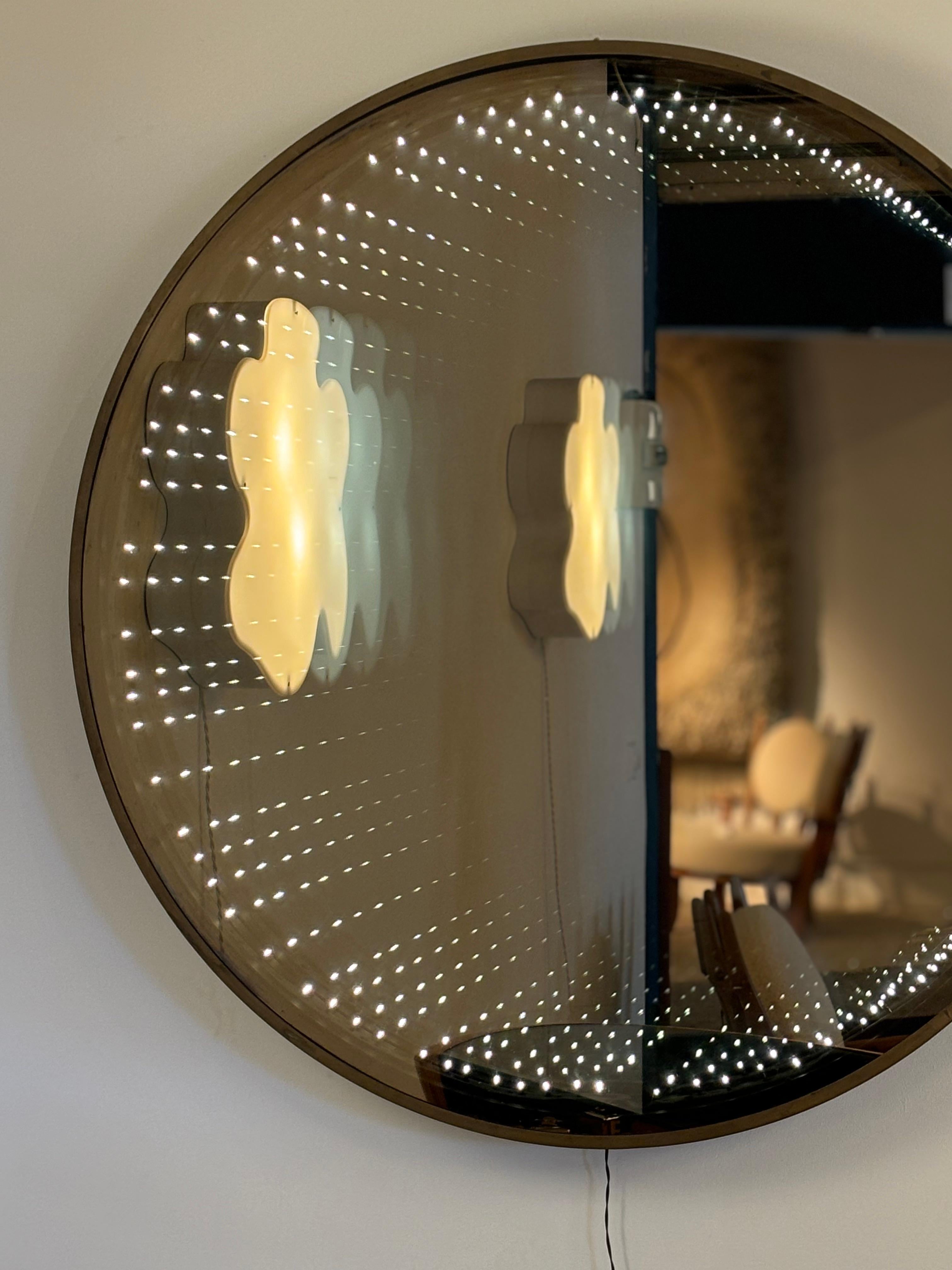 Questo grande specchio rotondo a sfioro degli anni '70 è un pezzo emblematico del fascino di quel decennio per la luce, la percezione e il design futuristico. Costruito con una struttura cromata e un sistema a doppio vetro che nasconde