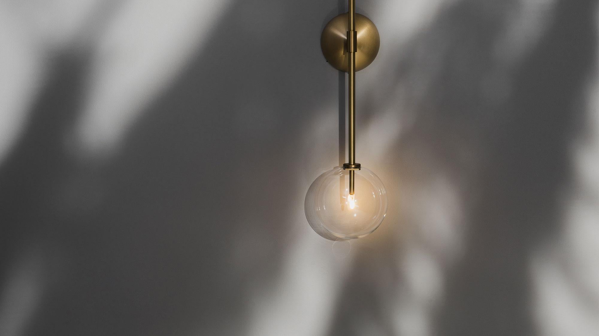 Two glass globes balance on either end of a single vertical arm, poised upon a conical brass mount. This stylish linear composition creates a balanced and minimalist impression.

Available in our three signature finishes: Lacquered Burnished Brass