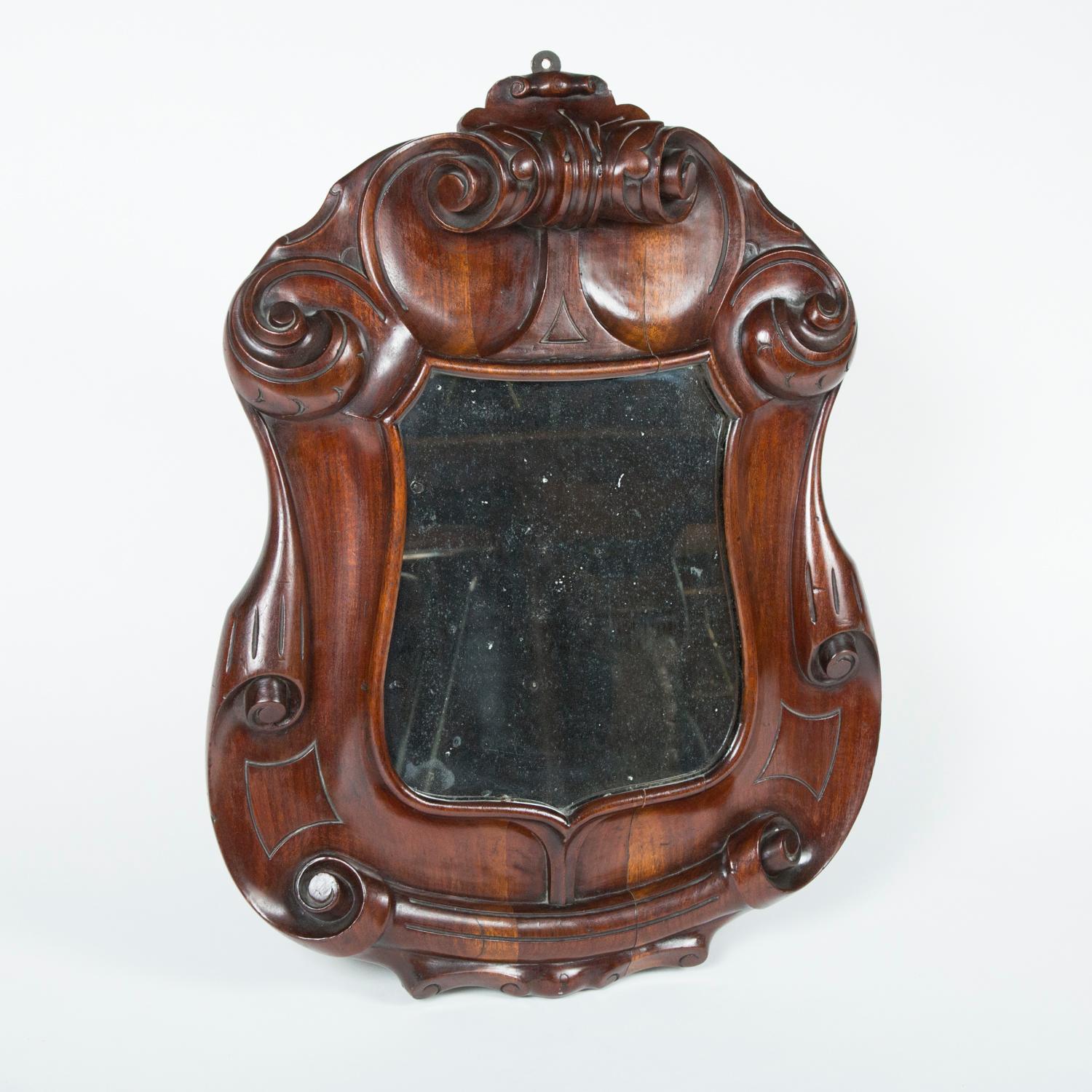 A well carved walnut mirror in the form of a heraldic shield.