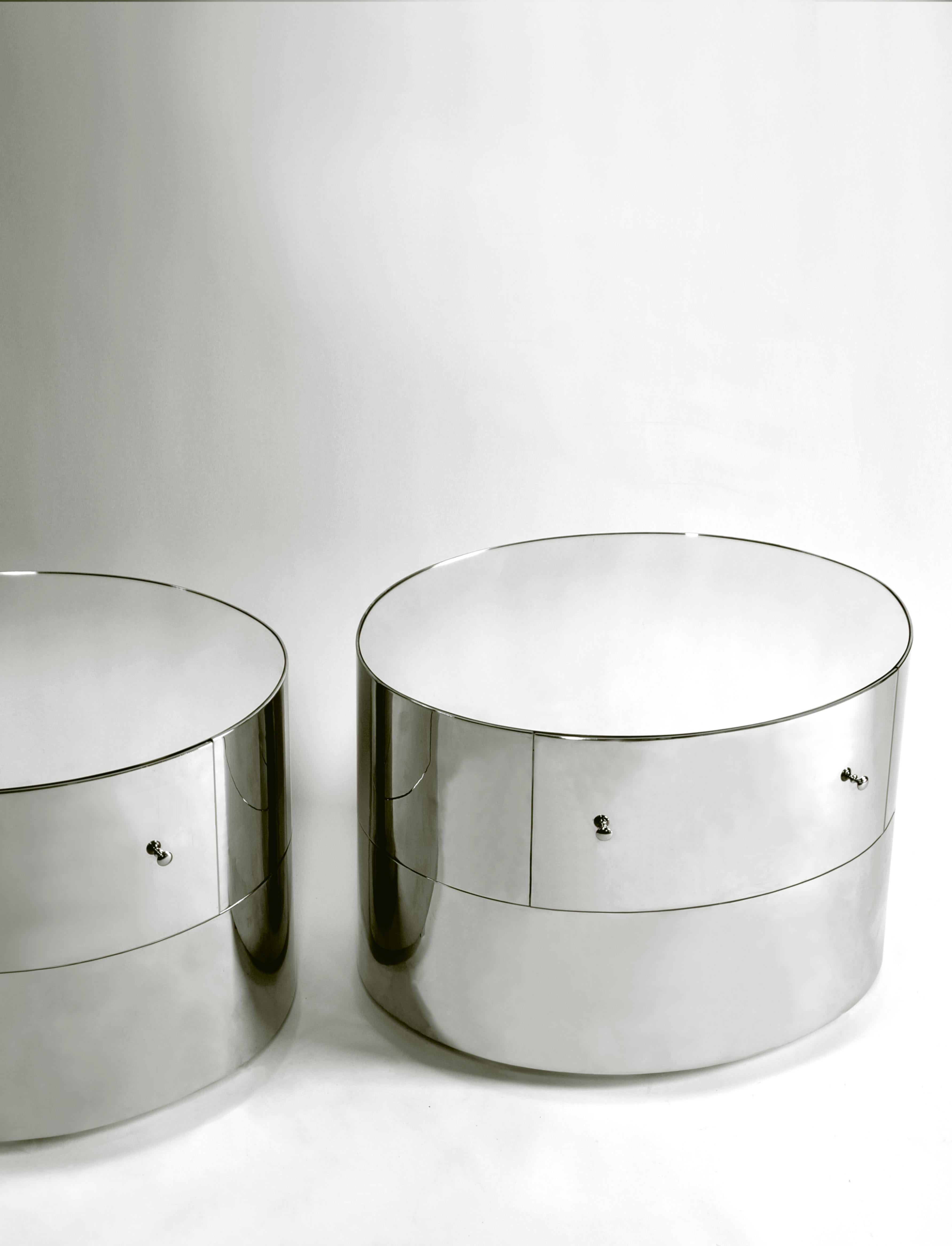 The mirrored side table has a distinct elliptical profile and is made from hand bent cold rolled steel. The metal exterior is twice dipped in chrome then nickeled for a subtle reflective color combination. An inlayed mirror sits flush within its