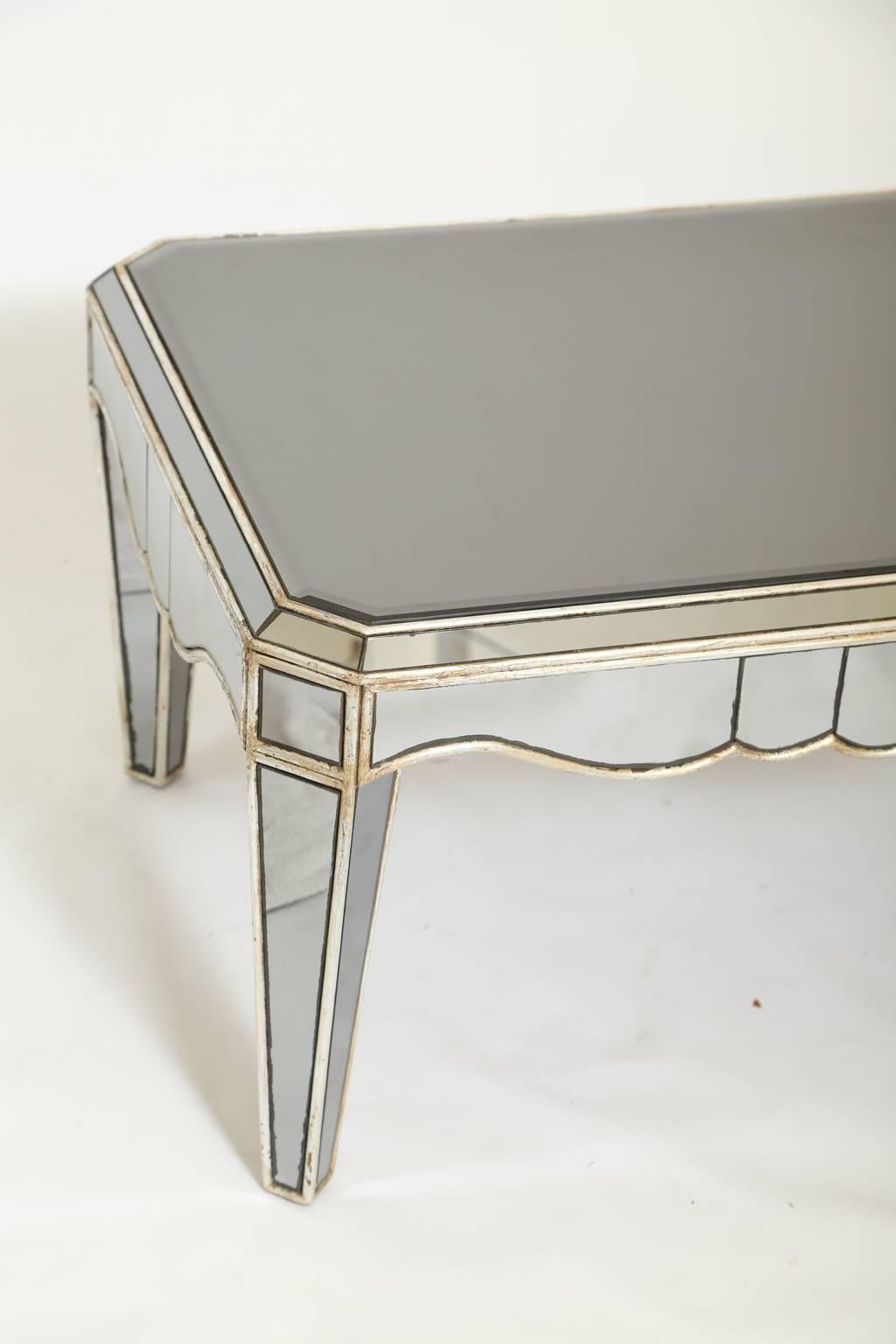 Coffee table with all of its surfaces covered in distressed, smoked mirror plate, bordered by silvergilt trims, its rectangular top on scalloped apron, raised on square-section, tapering legs. 

Stock ID: D1372