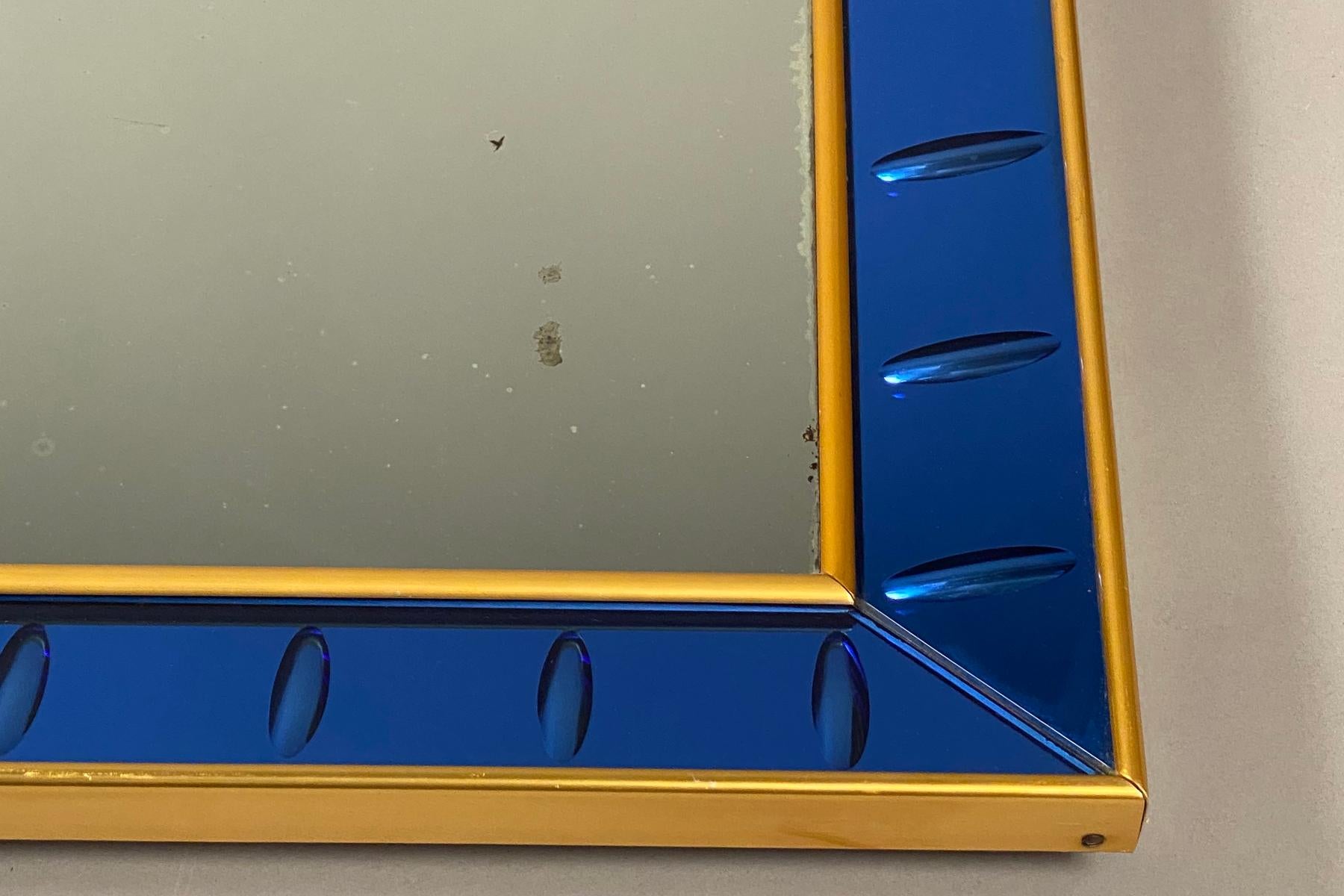 Rectangular mirror plate, framed with panels of similarly mirrored, blue colored glass with beveled edges, held in brass trim. Age spots in mirror plate consistent with the piece’s age.