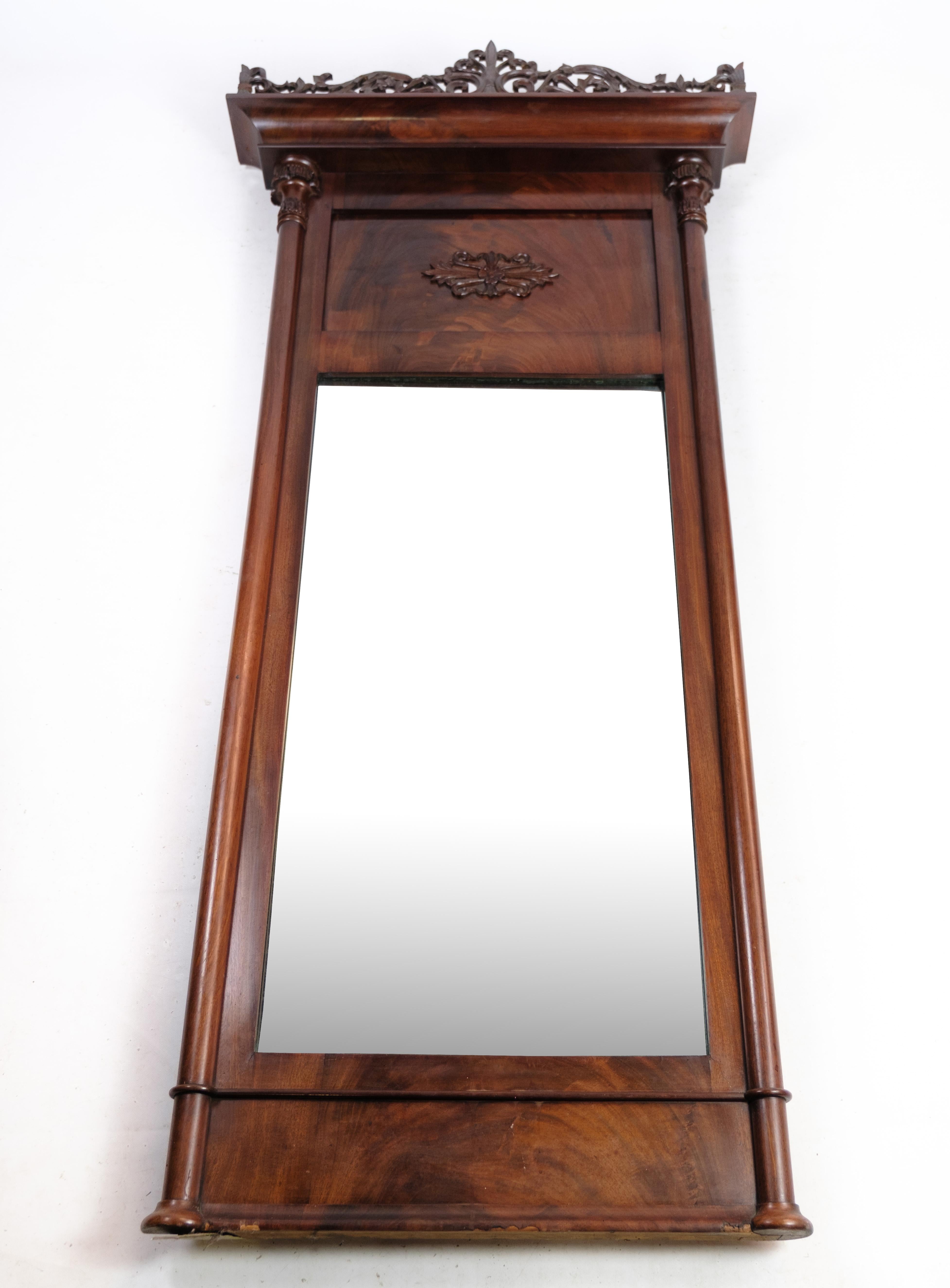 The mirror of hand-polished mahogany is a stunning piece from the late Empire period, hailing from Denmark around the 1890s. The rich, deep mahogany wood has been carefully hand-polished to bring out its natural beauty, and the frame is adorned with