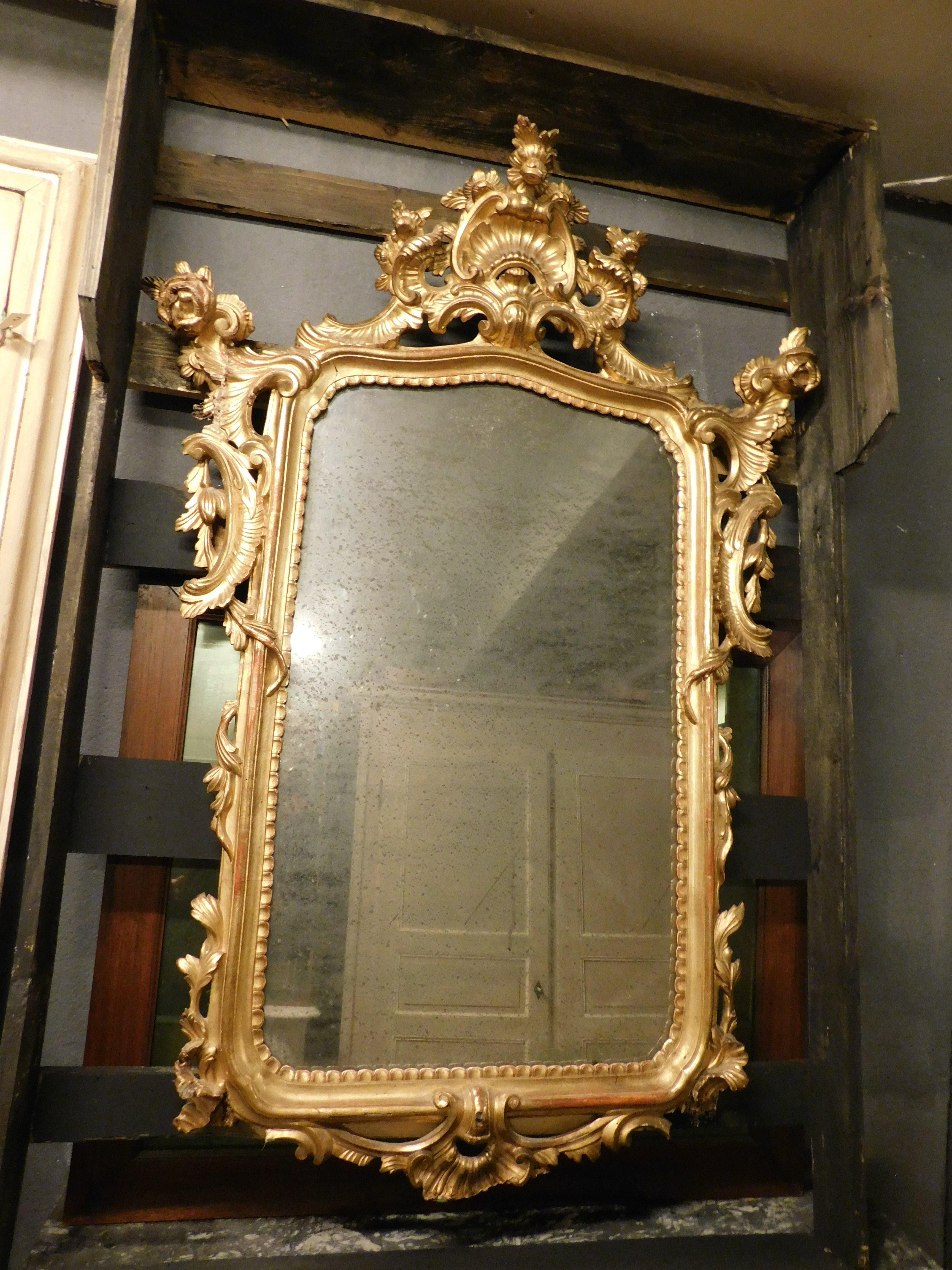 Antique and large mirror in lacquered and gilded wood, rich carved top with central shell and large floral decorations, from Italy, The floral and leafy decorations follow one another throughout the frame. Original from the 19th century.