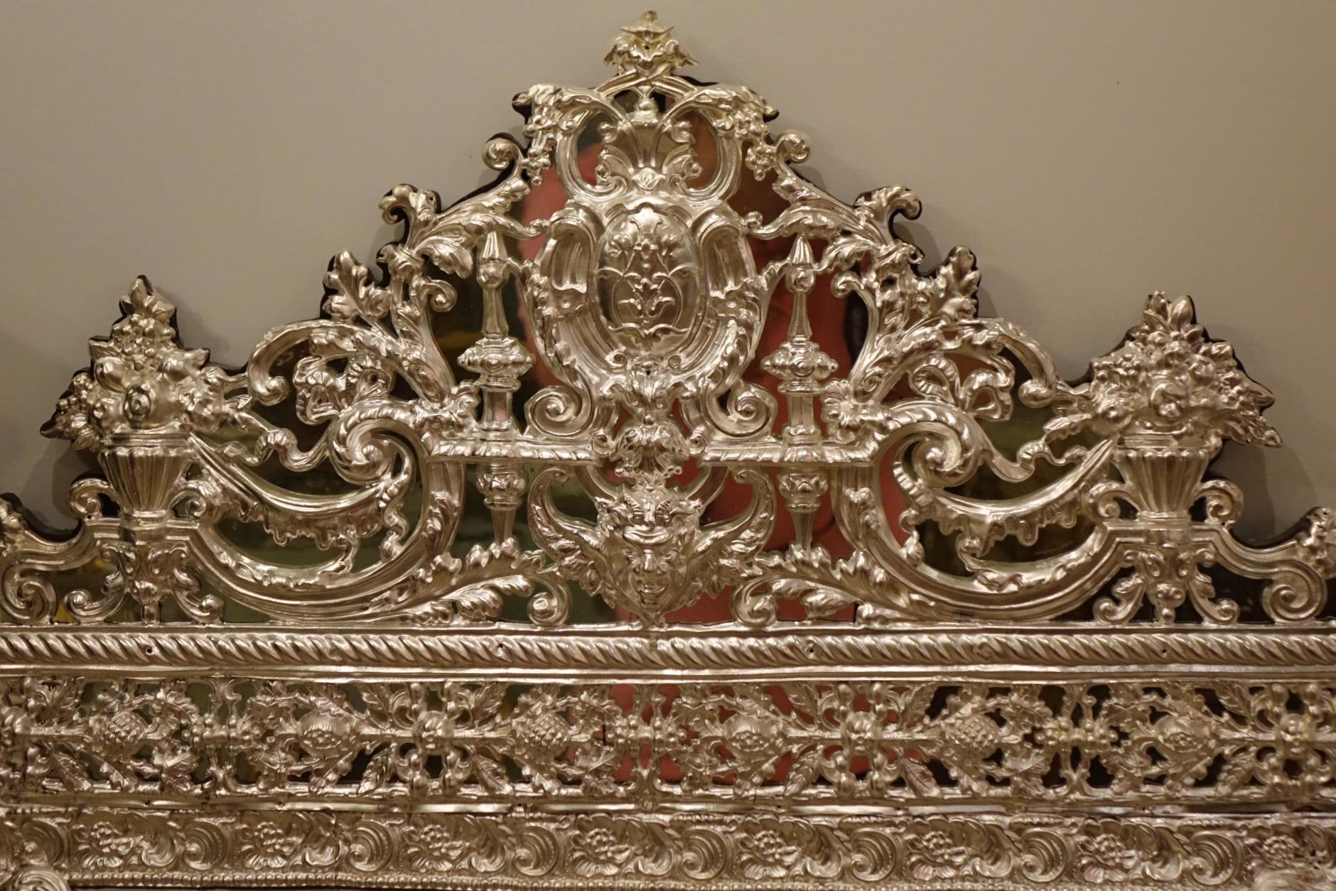 Mirror in Louis XIV style in embossed silver plated brass, France, 19th century.
French Second Empire period.
The central mirror, the parclose mirrors on the sides, and the pediment have beveled edges.
Decorated with scrolls, volutes,