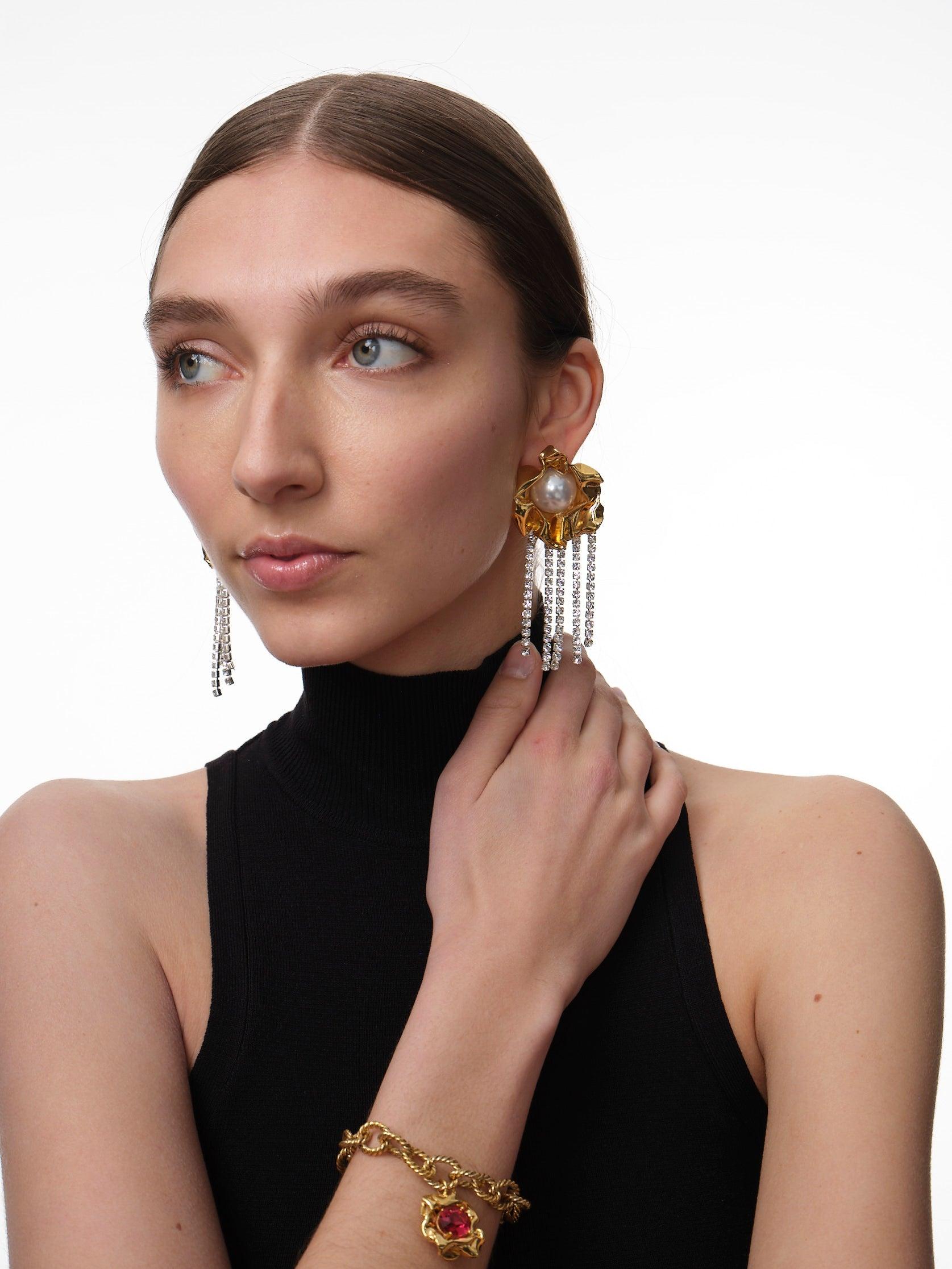 The Titania Pearl Earrings are statement earrings featuring an oversized faux pearl and dangling crystal fringe. Their intricate folds are crafted by hand and dipped in gold. Inspired by A Midsummer Night's Dream, these sculptural statement earrings