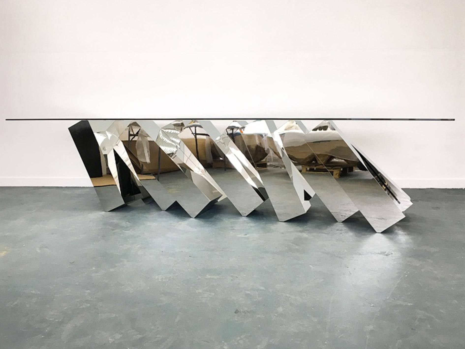 With its glass table balancing miraculously on top of a series toppling, mirror-polished monoliths, Duffy London’s mind-boggling creation appears to defy the laws of physics by remaining in a permanent state of impending collapse.

The monolithic