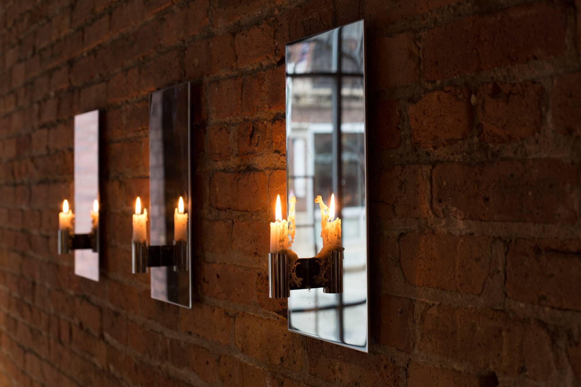 Strikingly simple and minimal, the contemporary, modern, asymmetrical candle wall sconce, made from mirror polish stainless steel, reflects the light doubling it’s effect which perfect on either side of a fireplace or painting or as a series along a