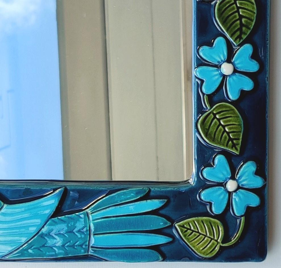 A mirror made of stamped clay, richly decorated with polychrome enamels in shades of blue, green and white. Mithé Espelt makes repeated use of this chromatic harmony. The use of bird and flower motifs is also recurrent. Here, the artist draws
