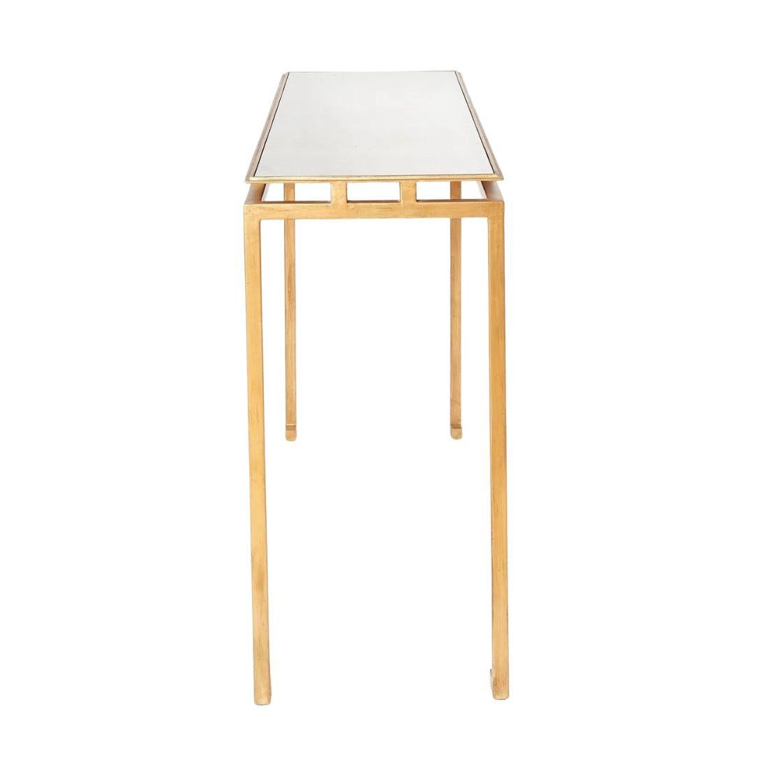 This elegant console table features a slender gilt metal frame with graceful, narrow legs and subtly stylized feet inspired by Asian design motifs. The mirrored top appears to float effortlessly above the base, lending a sense of lightness and