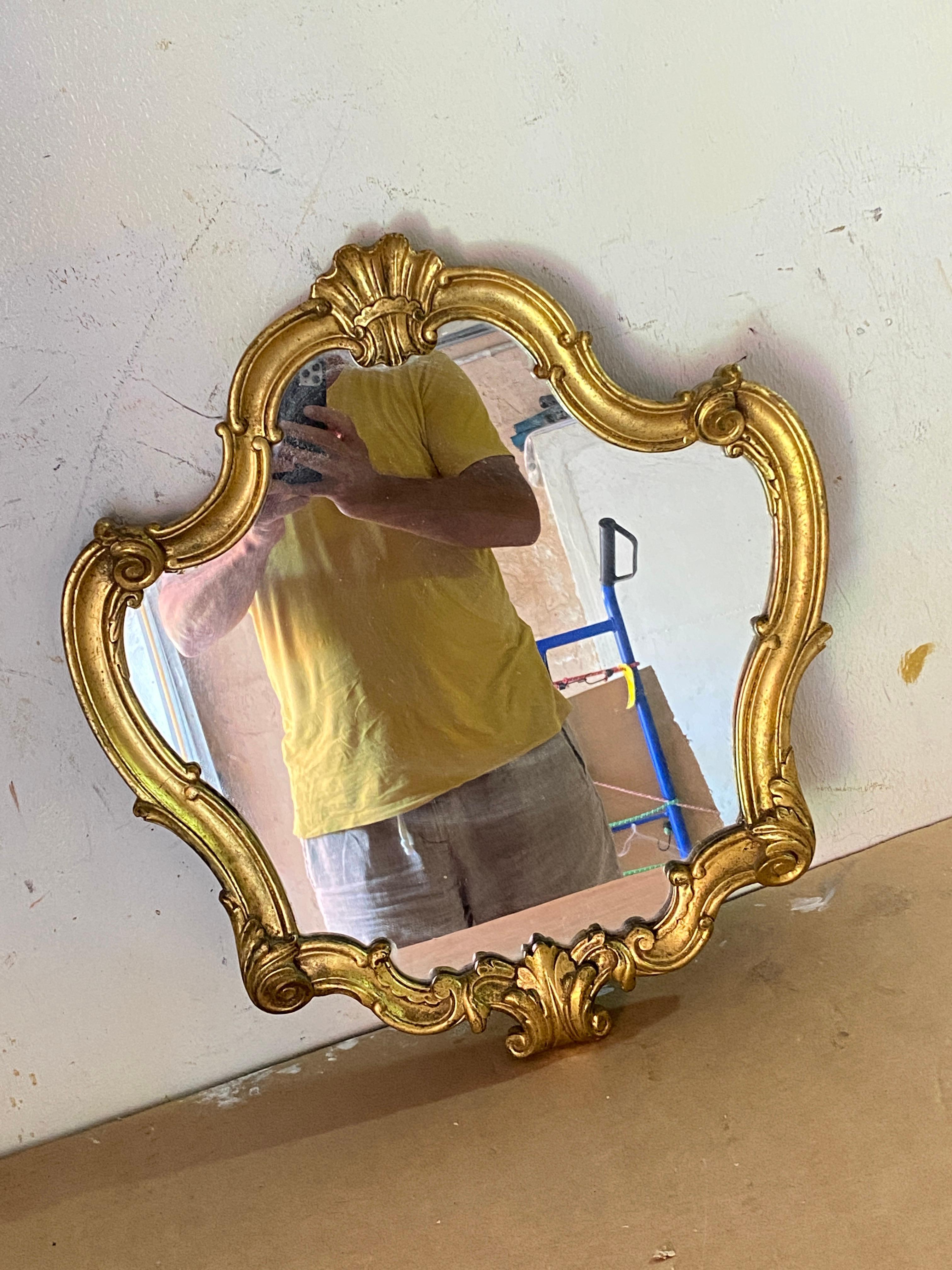 Carved, turned, and gilded wooden mirror with gold leaf. There is a label on the back which guarantees the authenticity of the gold leaf gilding. This wooden mirror was made at the beginning of the 20th century in France. Its color is that of gold.
