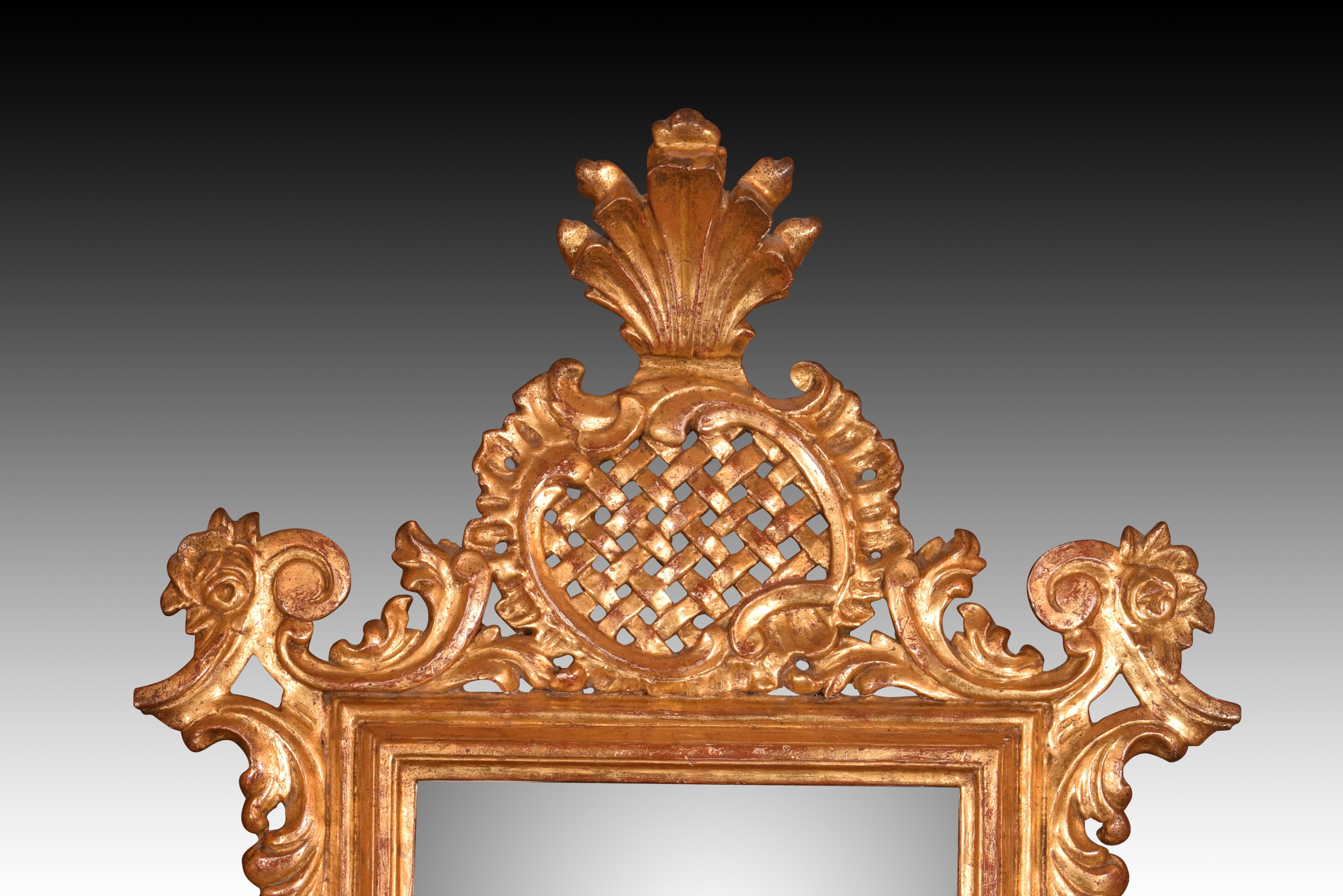 Miroir avec garniture en bois doré. Vingtième siècle. 
Miroir rectangulaire mis en valeur par un décor à base d'éléments végétaux sculptés et d'un motif de barres dans une forme végétale. Les courbes que dessinent les feuilles montrent l'influence