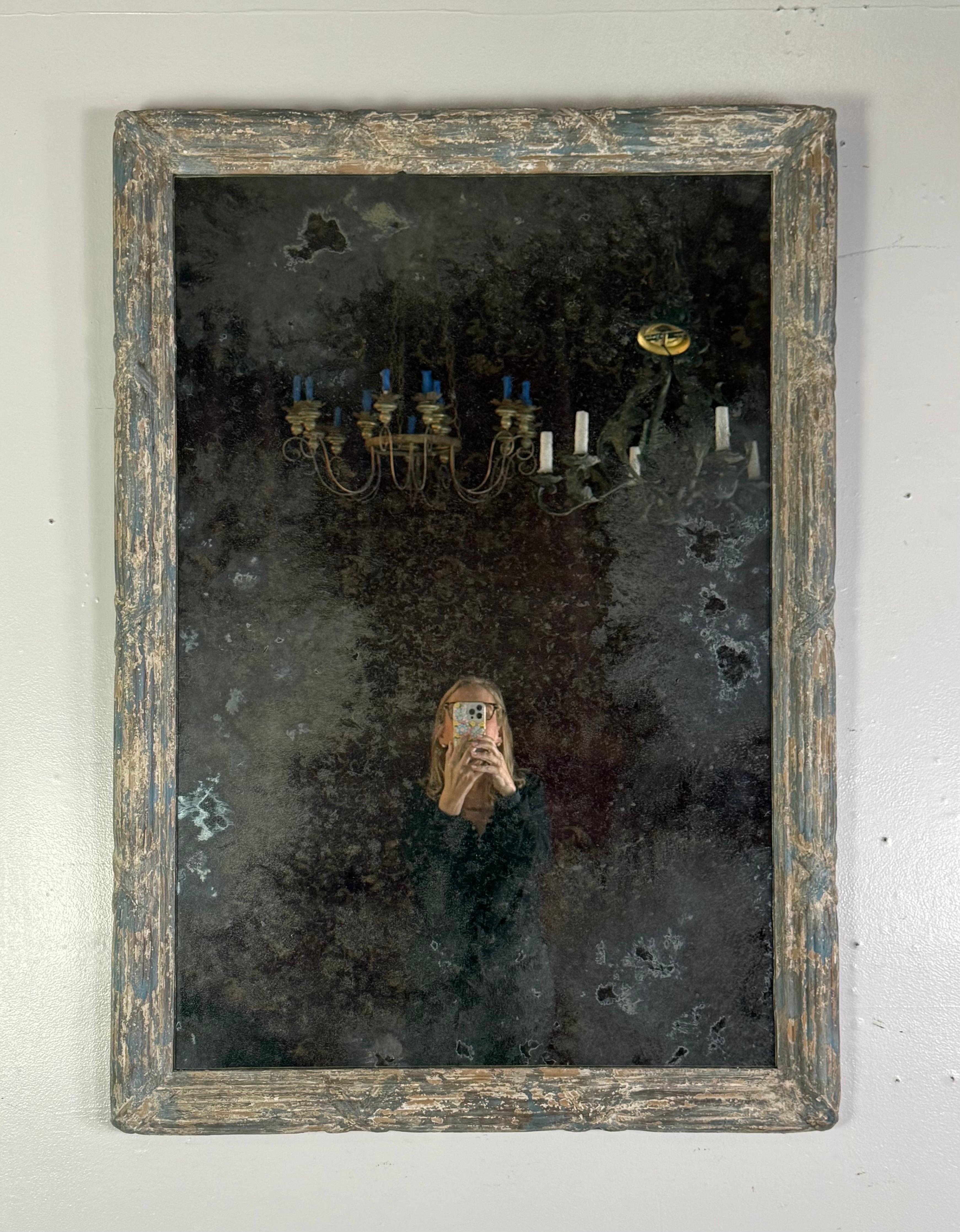 Este espejo tiene una belleza conmovedora y desgastada por el tiempo que habla de décadas de uso y envejecimiento natural. El marco rectangular es de madera y conserva restos de pintura antigua en capas -azules suaves y blancos cremosos- que se han