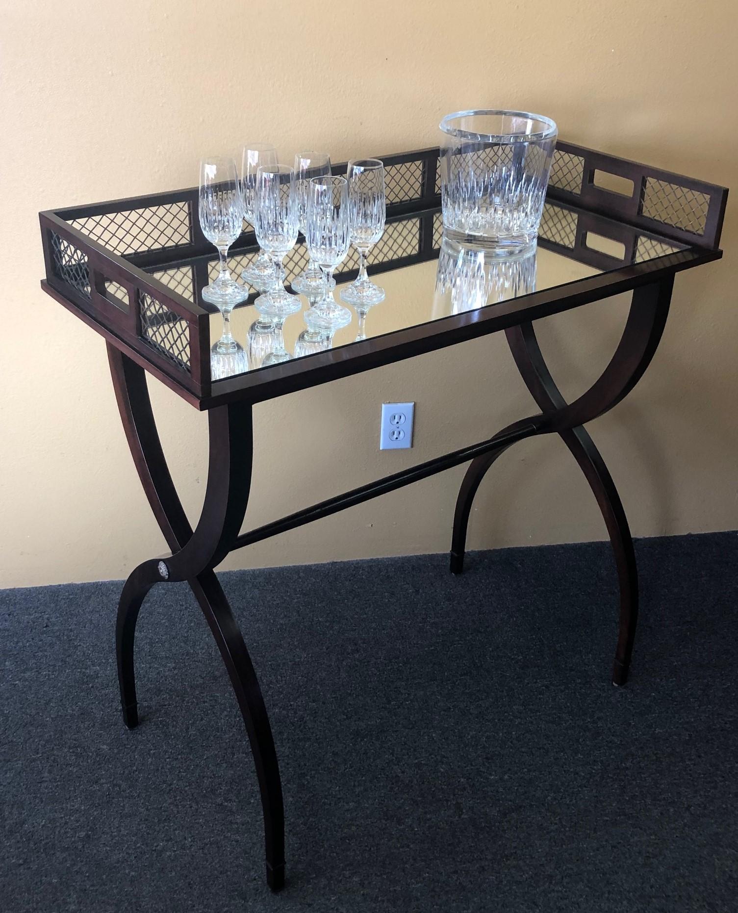 Fabulous drinks / cocktail tray table by Barbara Barry for Baker, circa 2000s. The two-piece mahogany drink table features a removable mirrored top tray with a wire mesh back splash and a arched leg stand with brass hardware. This is a very stylish