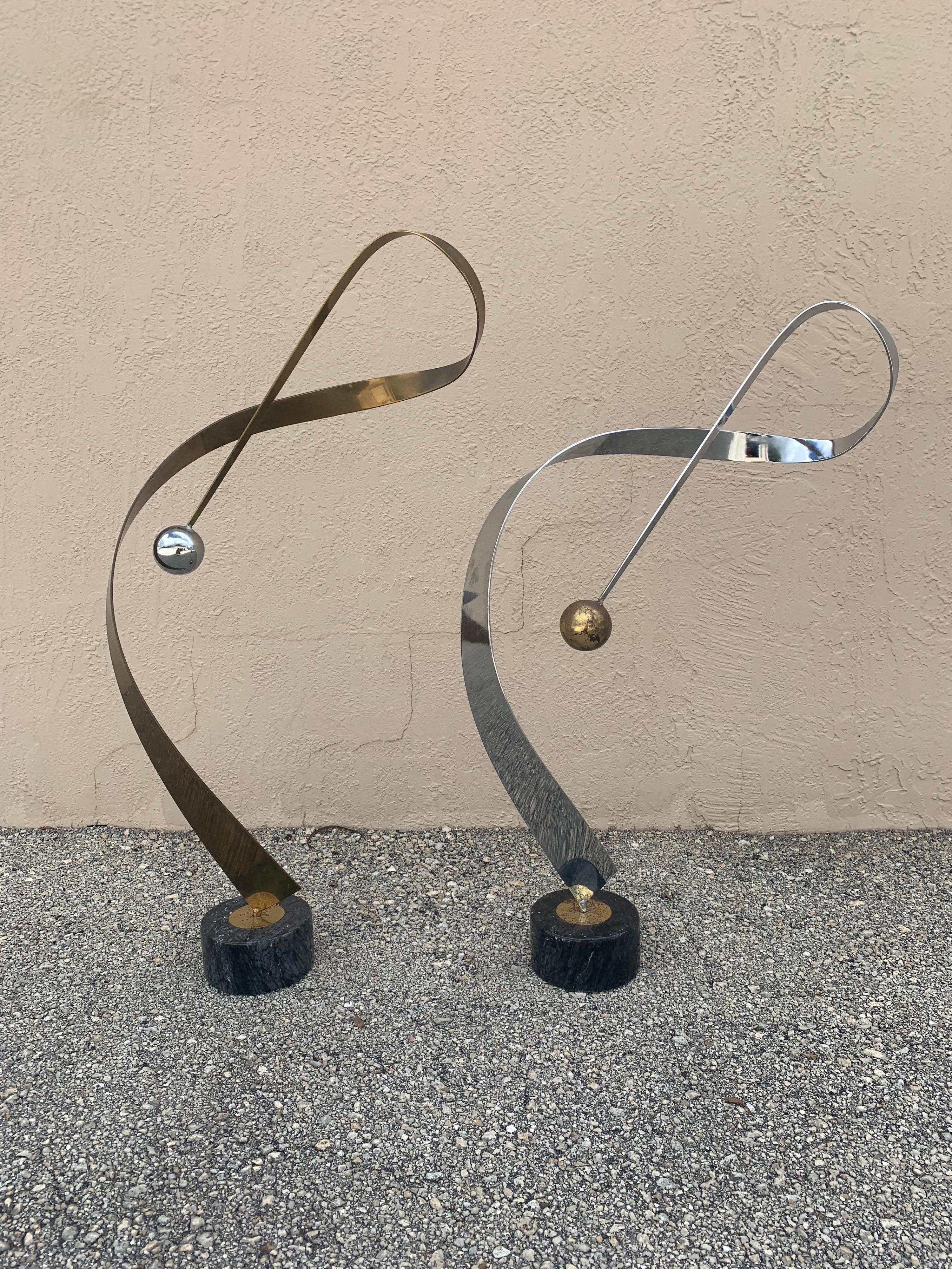 Stunning pair of mirrored Ribbon sculptures by C Jere. One sculpture is a brass ribbon with a chrome ball and the other a chrome ribbon with a brass ball. Both sitting on a black marble base. Beautiful and striking curves that change simply by