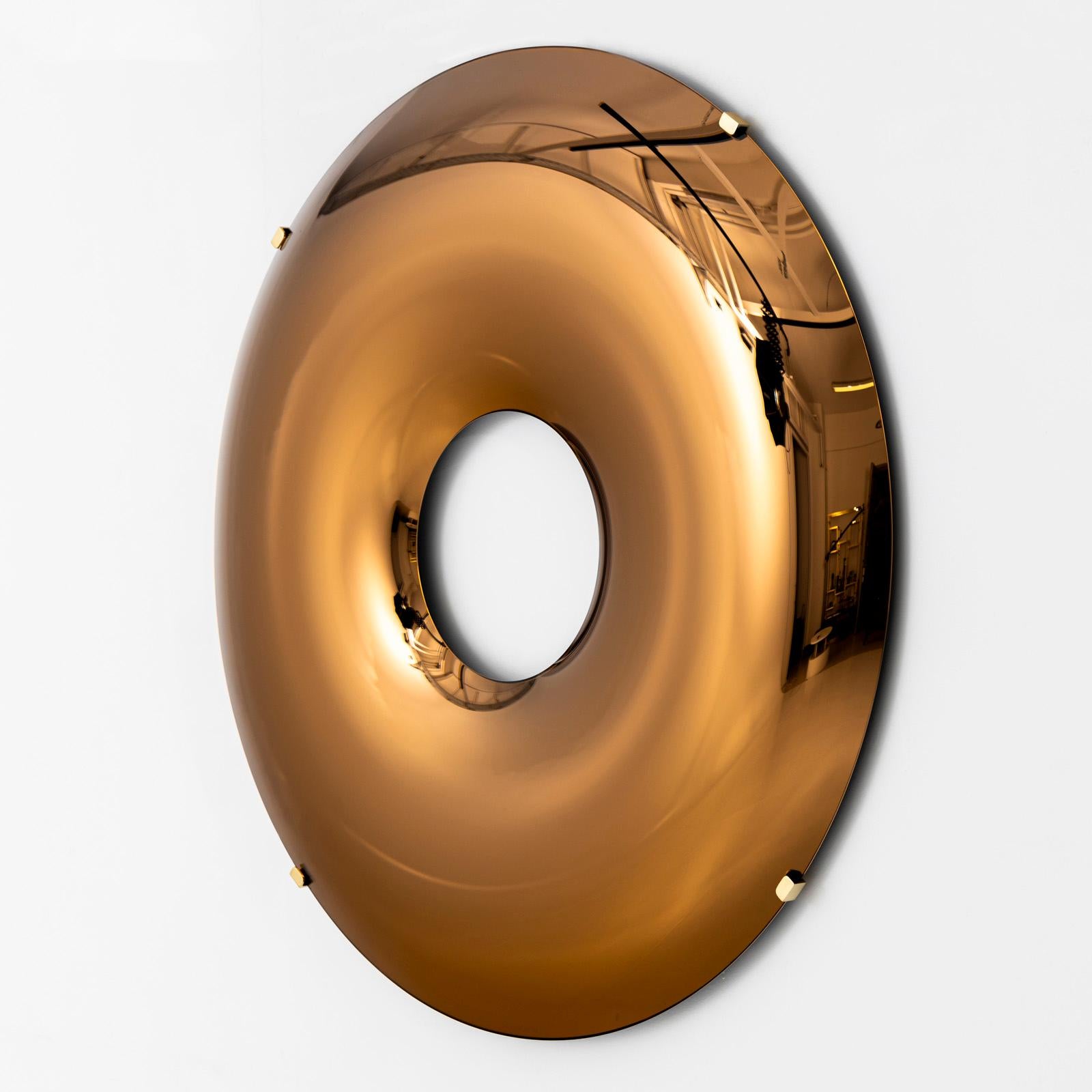 Grande oggetto da parete a forma di anello in vetro specchiato color rame. La lastra di vetro è convessa ed è sostenuta in tre punti da una staffa di ottone. 