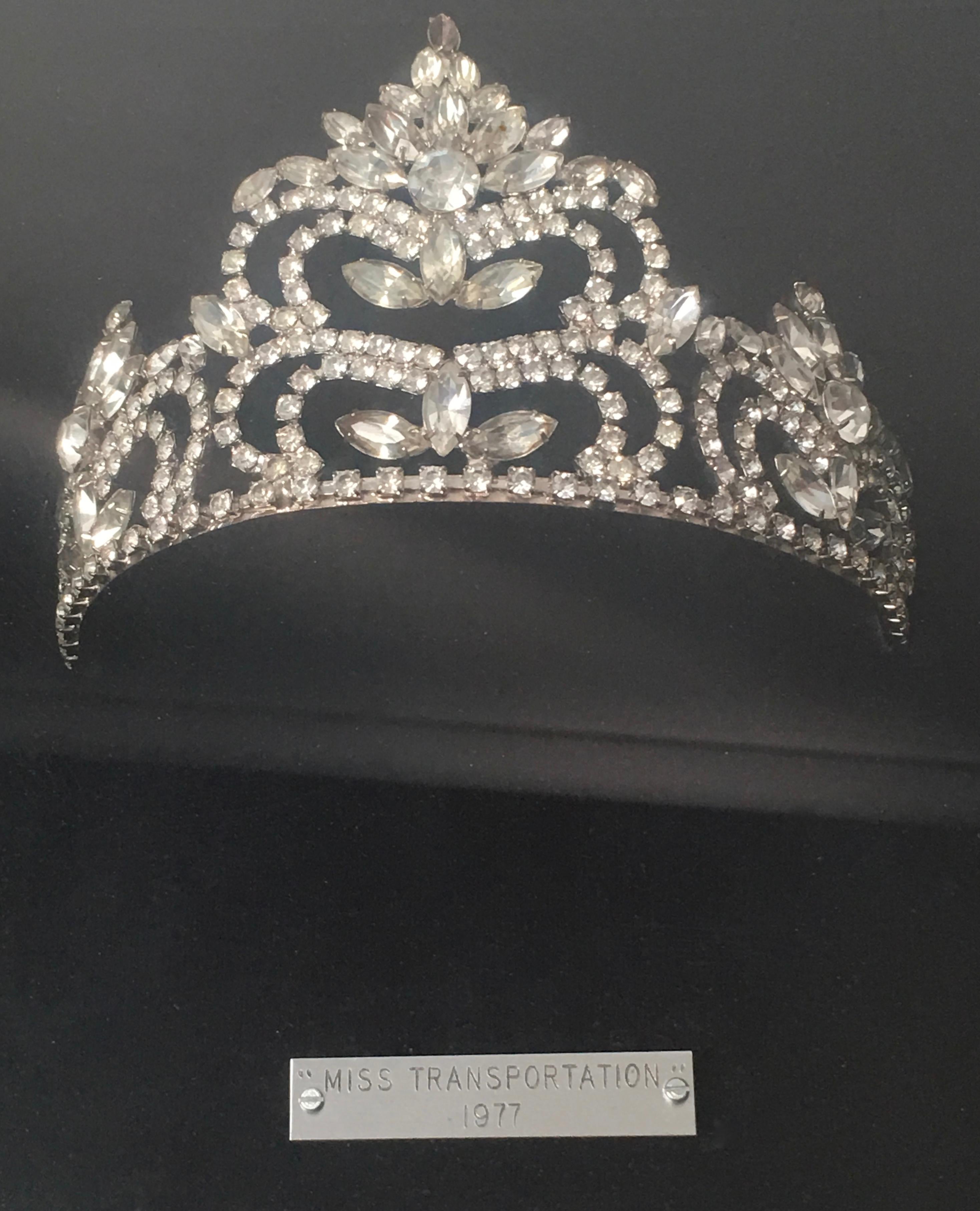 A rhinestone tiara which was used to crown Miss Transportation in 1977, mounted in a black velvet line deep shadow box with a silvered wood frame.