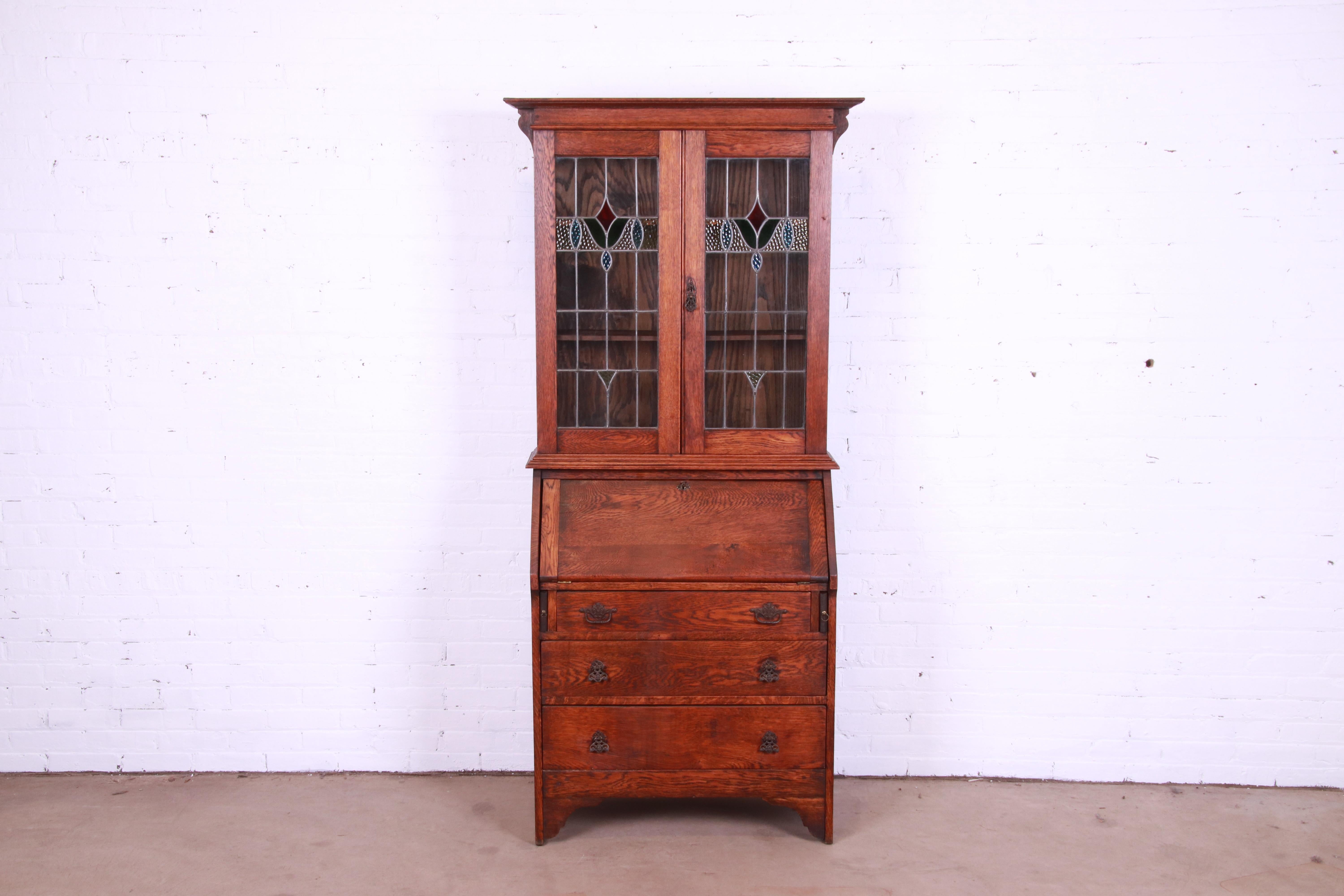 A gorgeous Mission oak Arts & Crafts drop front secretary desk with bookcase hutch

In the manner of Stickley

USA, Circa 1900

Solid oak, with multi-colored stained leaded glass panels and original brass hardware. Cabinet locks, and key is