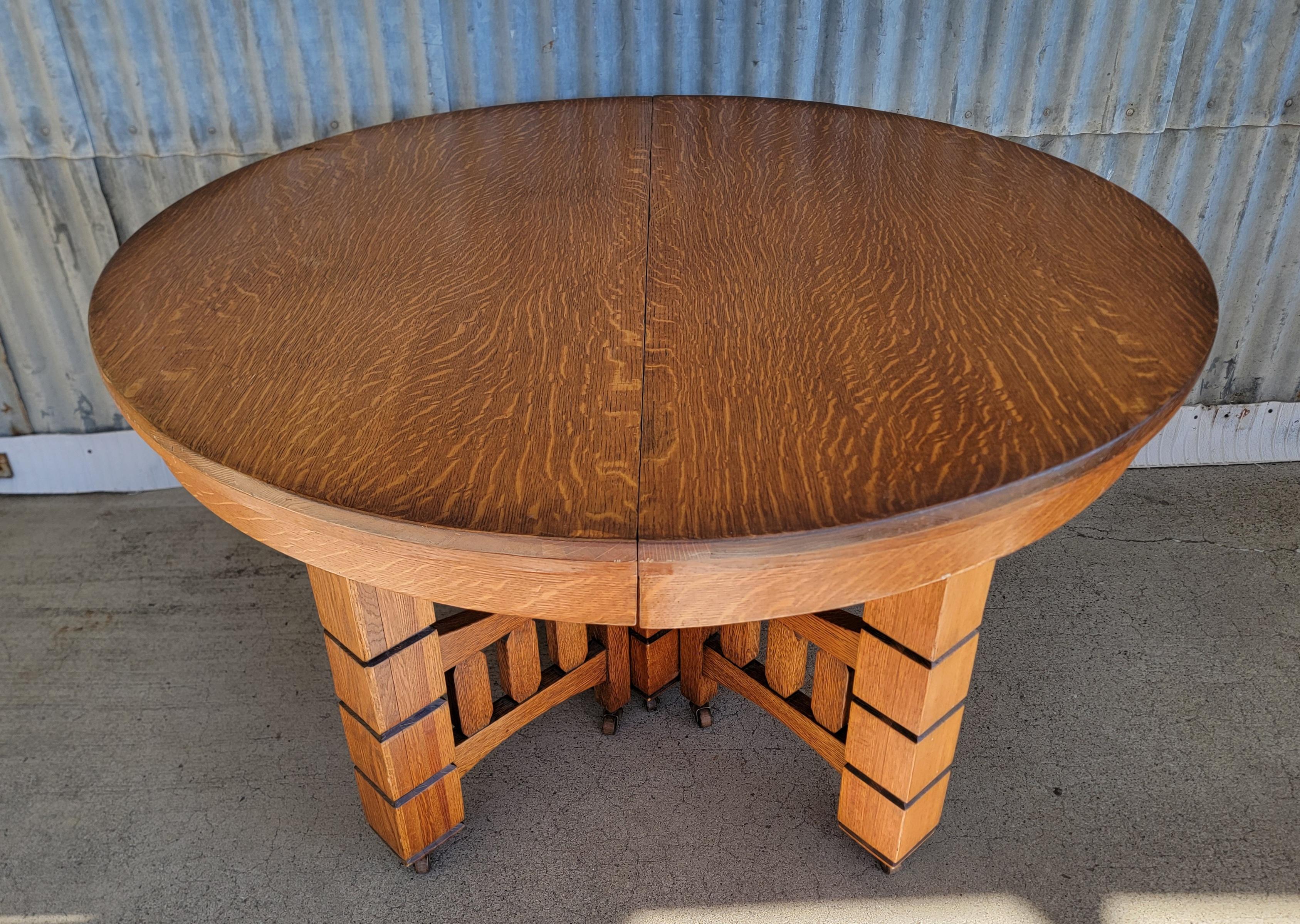 A period Arts & Crafts (Mission Oak) expanding circular dining table. Includes four 11.75 inch solid oak table leaves. Beautiful quartersawn / tiger oak wood grain. Original casters. Unusual detailed pedestal base. Retains several paper labels 
