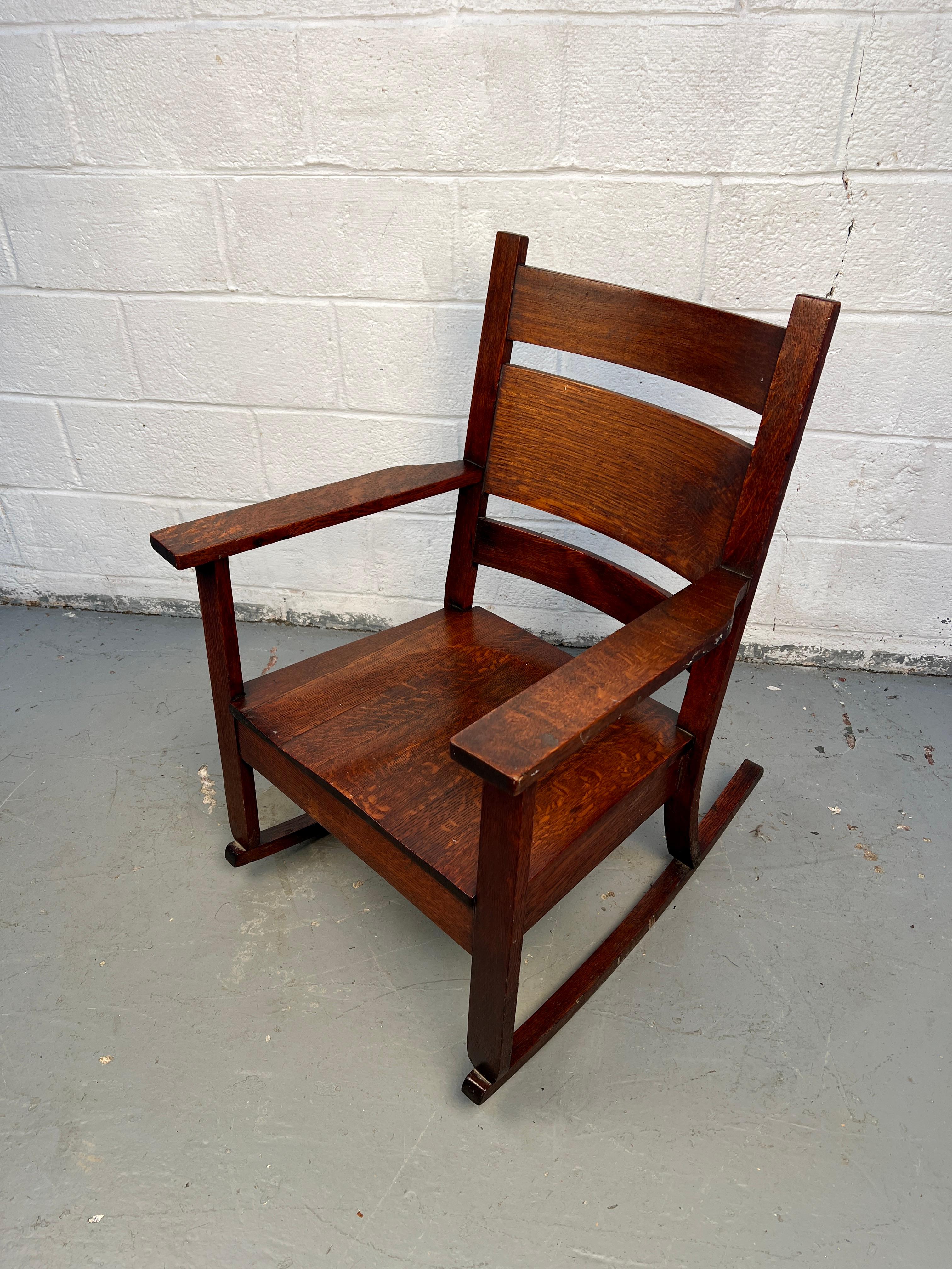 Klassischer Schaukelstuhl aus Eichenholz im Missionsstil, der in der Tradition von Stickley gefertigt wurde. Die Konstruktion aus massivem Eichenholz, die vertikalen Lamellen und die reiche, warme Oberfläche zeugen von zeitloser Handwerkskunst und