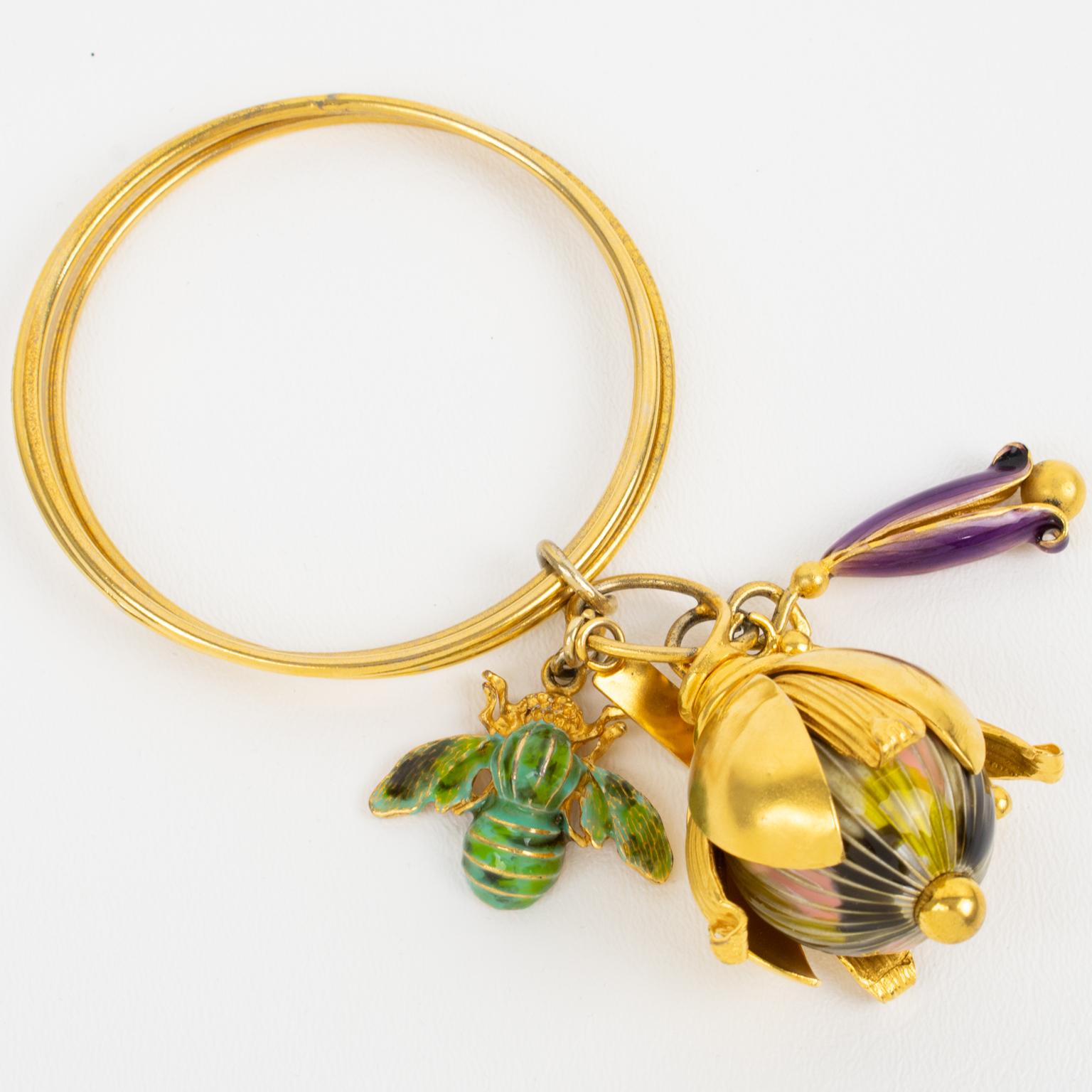 This romantic Missoni, Italy bangle bracelet features a trio of gilded metal thin band bangles ornated with floral dangling charms. The dangle elements are a huge and small flower, complimenting a bumble bee. The enamel colors are assorted green,