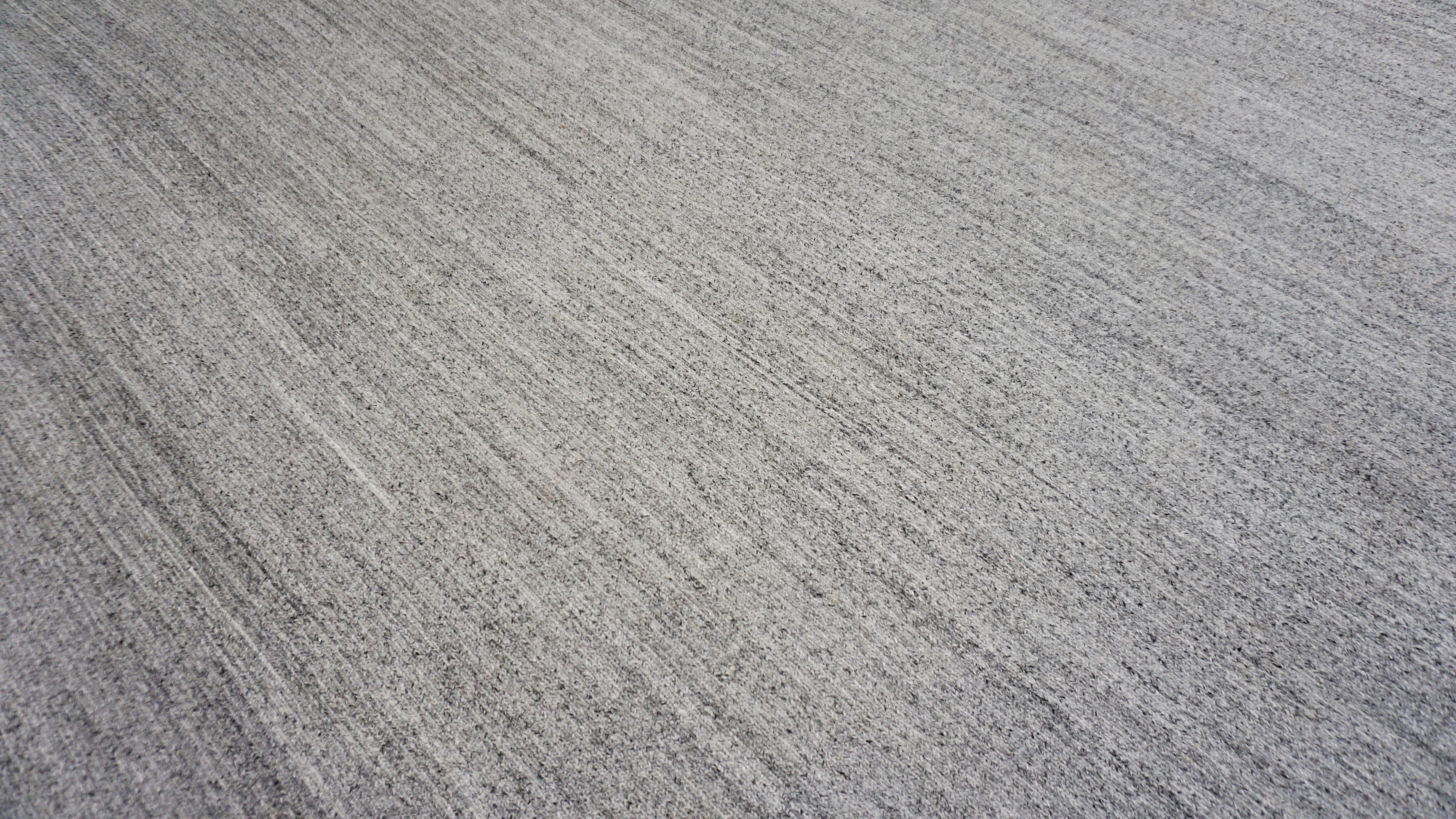 This handwoven Soumak rug in a silver grey wool-viscose blend evokes the serene calm of early morning mist. Expertly crafted by artisans, its surface reveals delicate tonal striations that shimmer subtly with movement—thanks to the interplay between