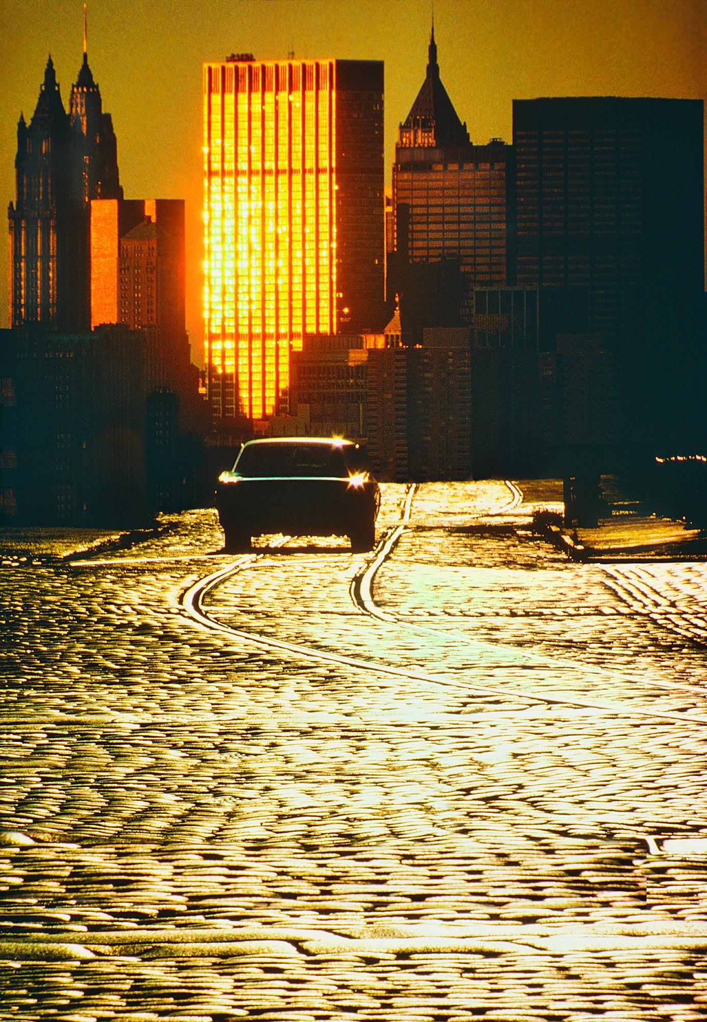 Color Photograph Mitchell Funk - La ligne d'horizon de Cobblestone Road au Lower Manhattan en lumière dorée 