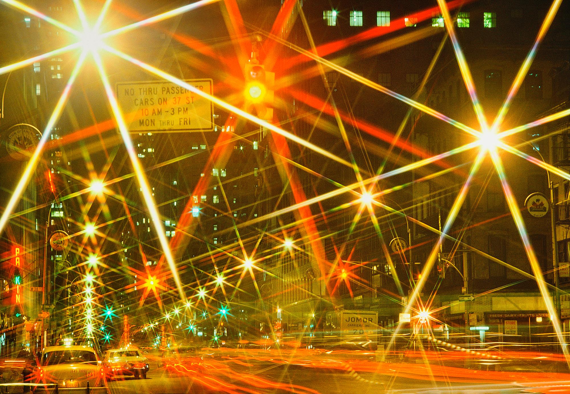 Streetlights on Manhattans' Sixth Avenure transform into a starburst of kaleidoscope color through an act of creativity from Photographer Mitchell Funk.  The emanating   light is a metaphor for the hustle and bustle energy of Midtown traffic.  
This