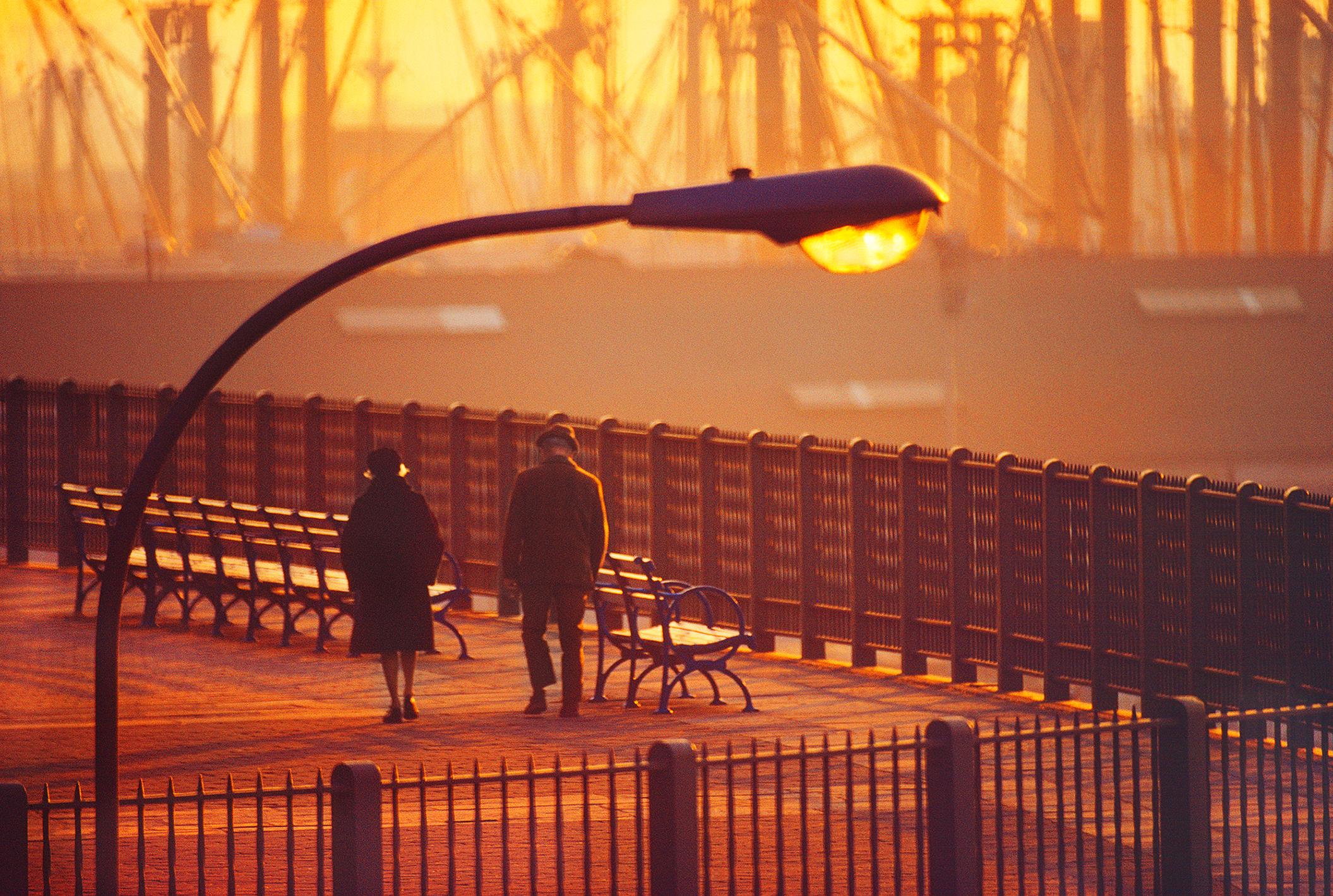 Old New York, Brooklyn Heights Promenade, 1972, in magisches goldenes Licht getaucht.  Es entsteht ein Gefühl der Einsamkeit, das an die Gemälde von Edward Hopper erinnert, in denen die kleinen Figuren von der Umgebung in den Schatten gestellt