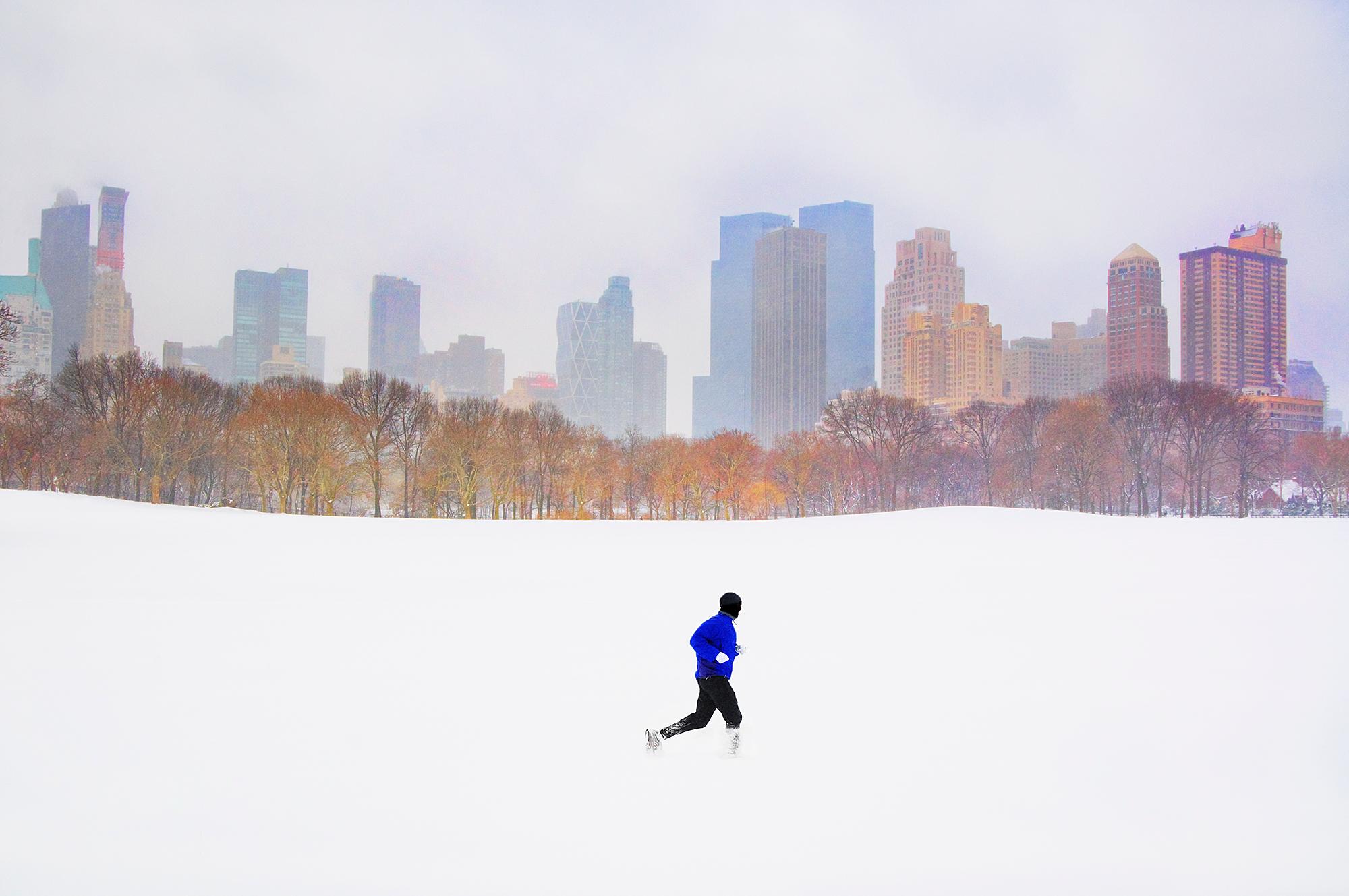Auf einem weiten Blick über eine der am dichtesten besiedelten Städte der Welt ist nur eine einzige Person zu sehen.  Ein einsamer Läufer, umgeben von weißem Schnee, wird von der Skyline des New Yorker Central Park South eingerahmt.  Seine