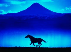 Caballo solitario corriendo silueteado contra la montaña azul