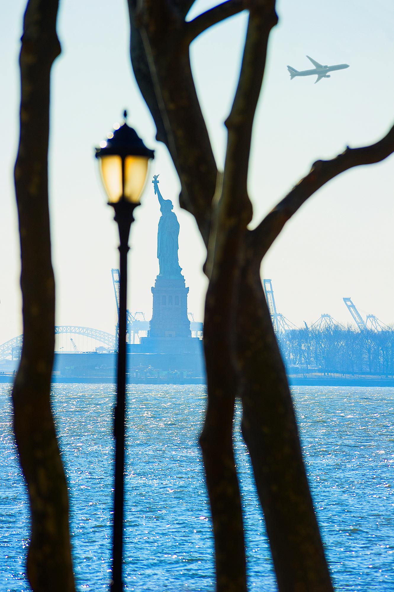 Liberty- Freiheitsstatue  Gerahmt von Bäumen und Straßenlampe im Battery Park,  New York 