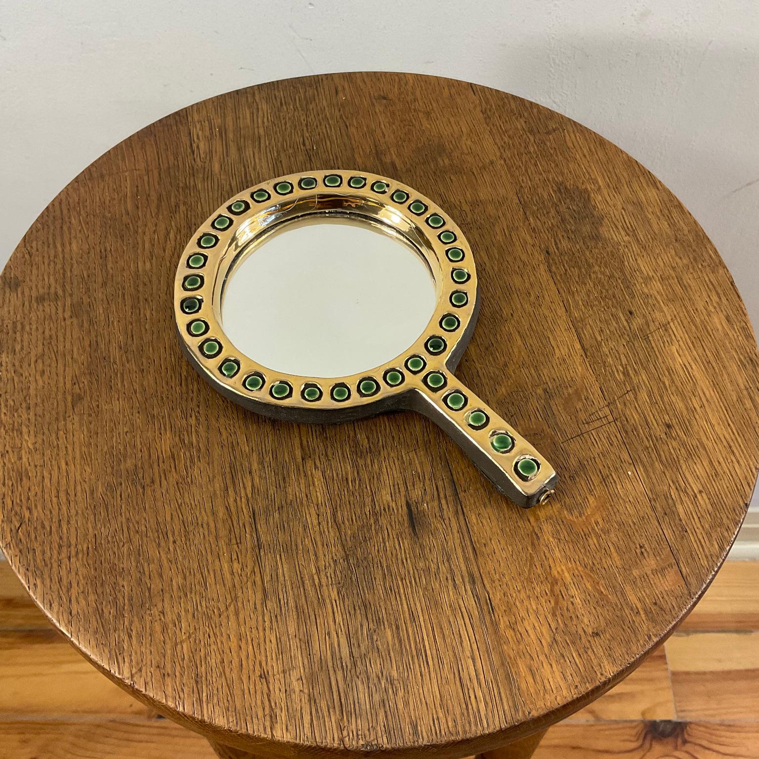 Rare hand-faced mirror designed by one of the greatest French ceramists Mithé Espelt (1923-2020) “Quadrille” model circa 1952.
Gold enameled terracotta with cracked green cabochons. Back covered with green felt.
Similar model ( with blue enamel