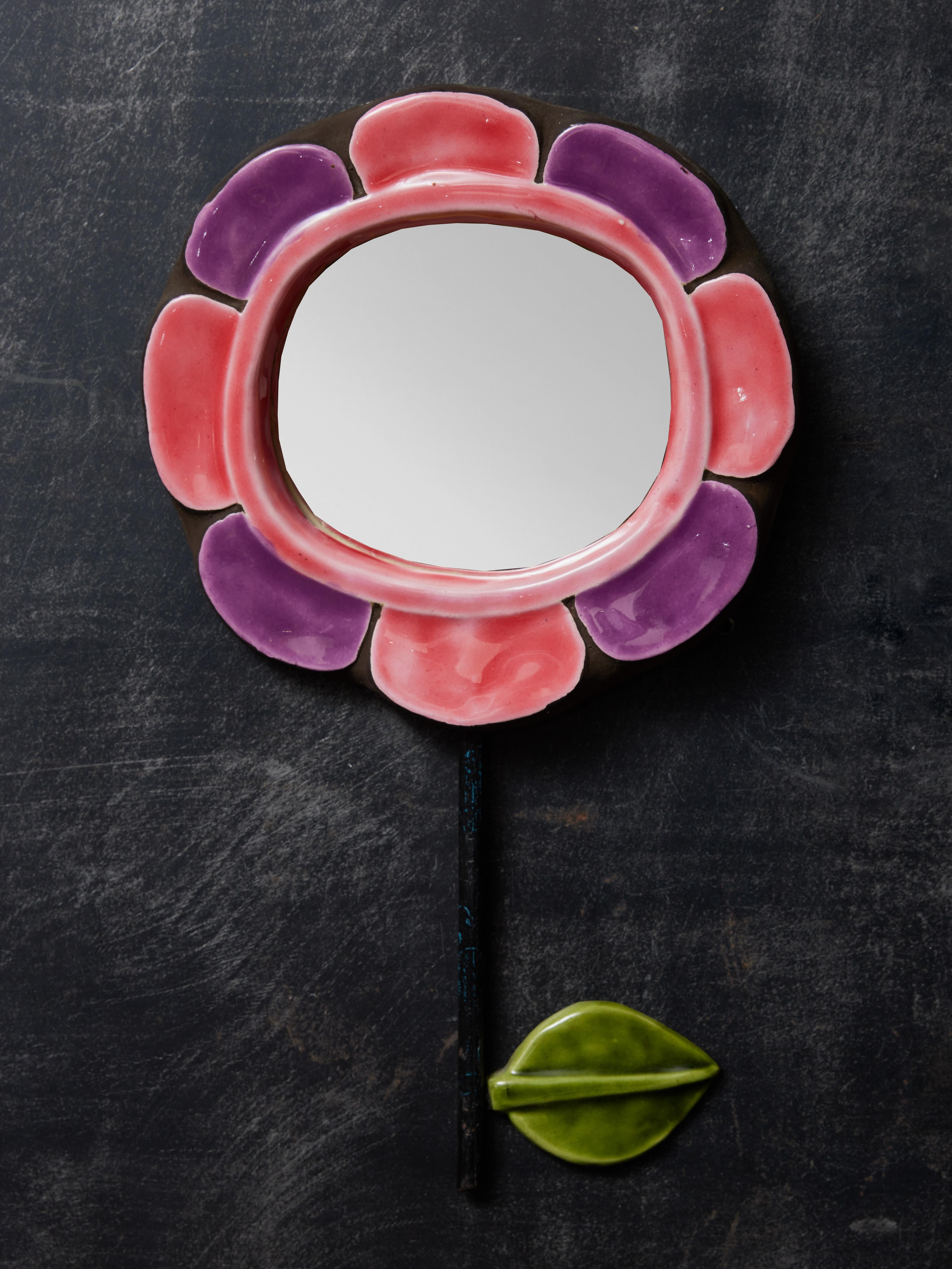 Miroir en céramique en forme de fleur avec des pétales roses et violets. Tige verticale en métal sur laquelle est fixée une tige de couleur verte.  feuille de céramique. Réalisé par Mithé Espelt.

Marie Thérèse Espelt, alias Mithé Espelt