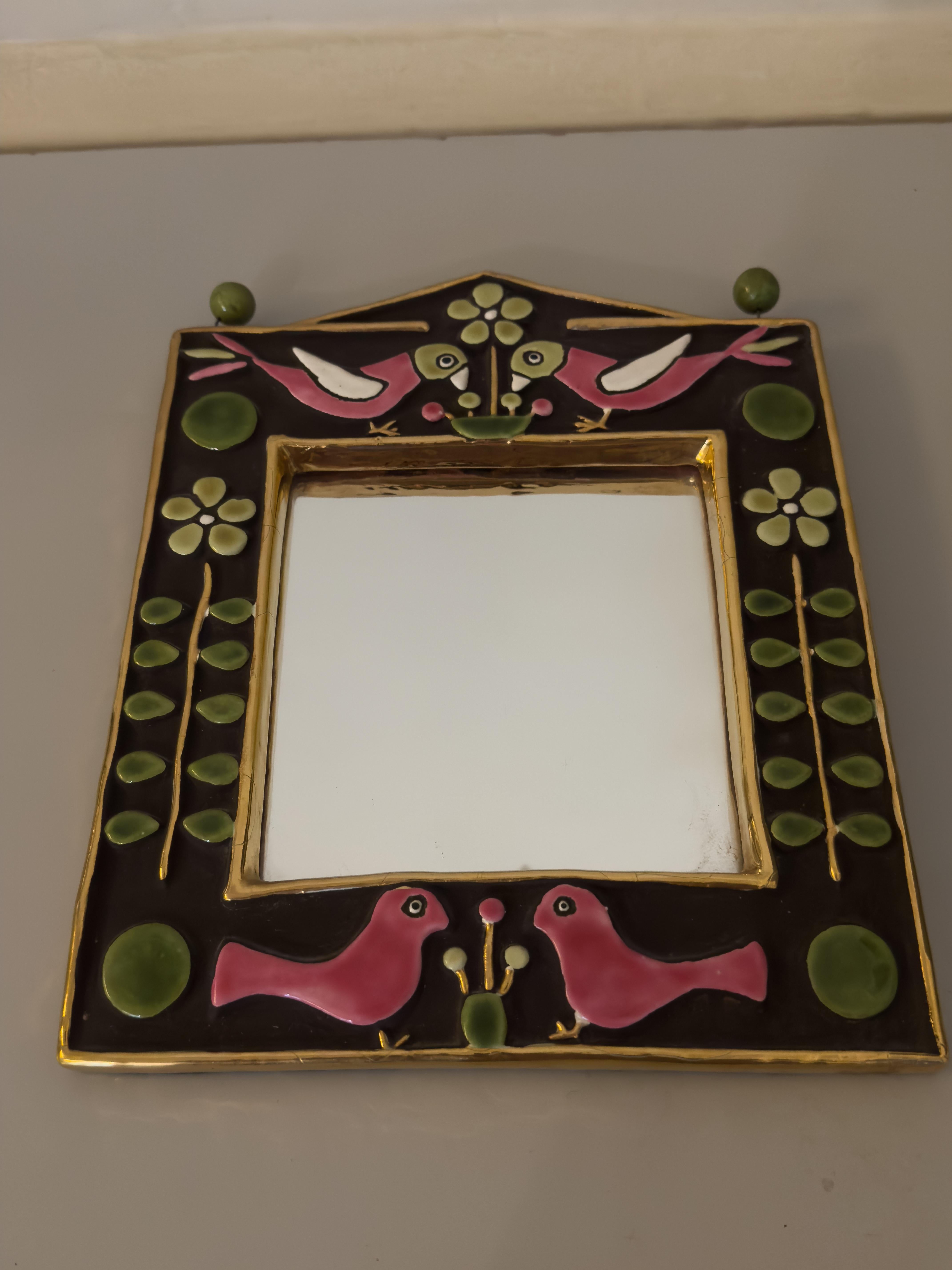 Ceramic wall mirror with birds and flowers (around the 1970s) by Mithé Espelt. A decorative piece surmounted by two pairs of enamel birds above and below the square mirror. The mirror is framed by a golden glaze that also forms the outer frame.