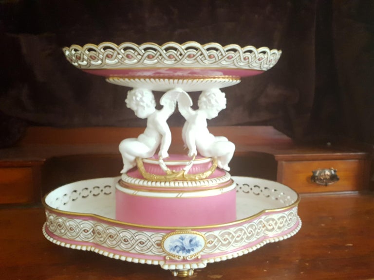 This is a magnificent centre piece tazza made by Minton in 1891, which was the Victorian era. The piece is made in white and pink porcelain where the base is quatrafoil in shape and the top is oval. The oval top has a reticulated or pierced