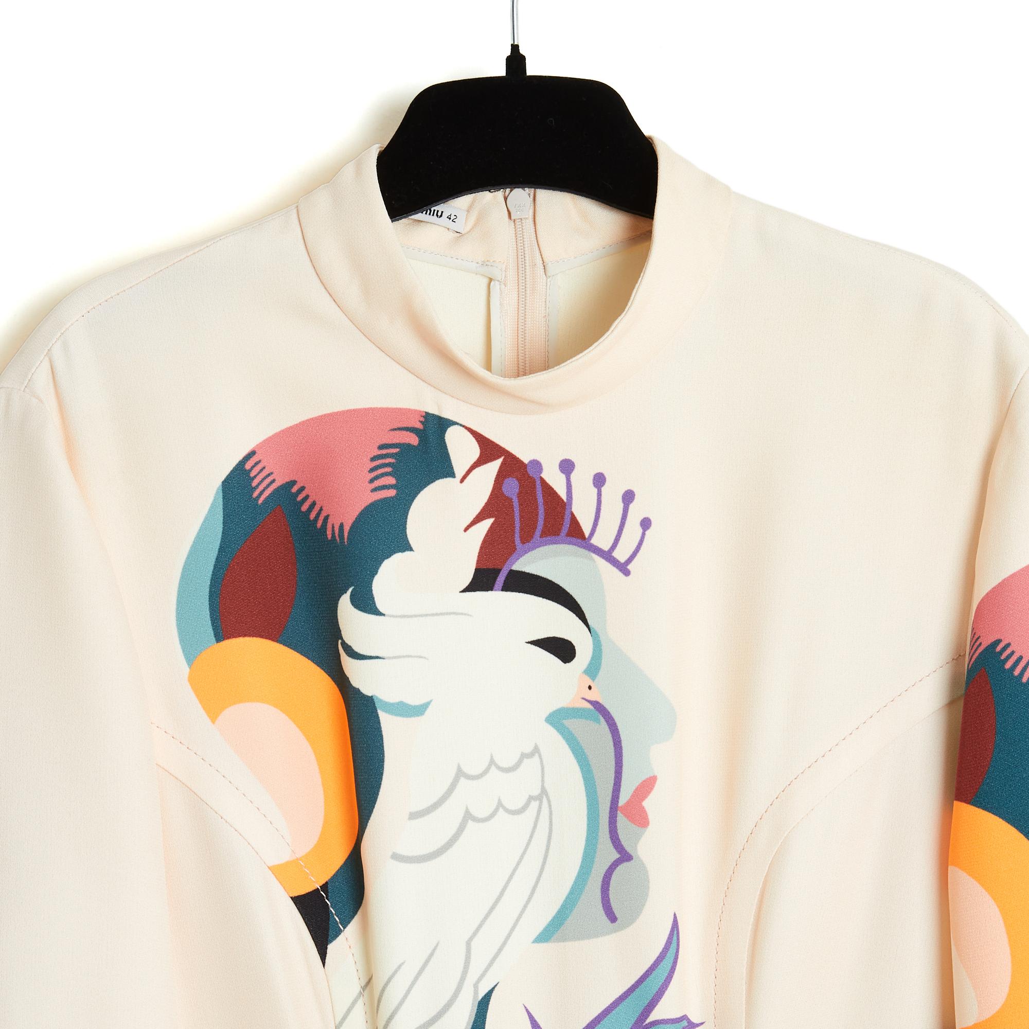 Robe Miu Miu de la collection printemps-été 2011 en crêpe viscose écru de couleur crème imprimé d'un motif associant un visage de femme et un oiseau, col rond fermé par un crochet et un long zip dans le dos, détails de surpiqûres à la taille, 3 plis
