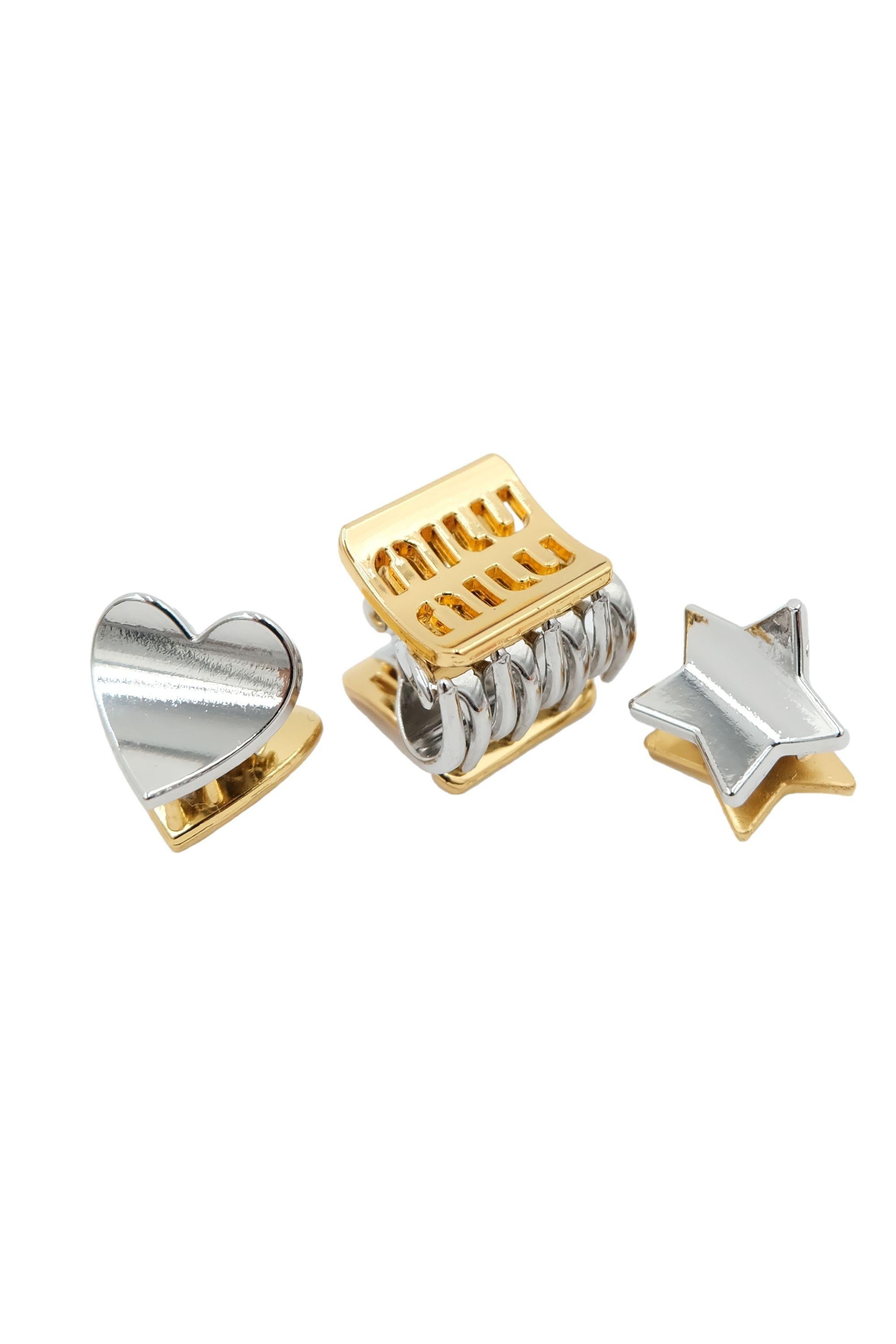 These Miu Miu mini hair clips are a playful and stylish accessory set featuring a mix of silver and gold-tone metal finishes with rhinestone embellishments. The set consists of 3 shapes, a heart, star and square claw clip. The face of each clip