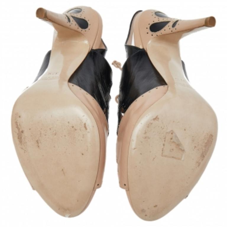 Estas sandalias Miu Miu son un reflejo del inmaculado arte de la marca en la fabricación de calzado. Fabricadas en piel beige y negra, estas sandalias tienen lazos de encaje, hebillas y recortes. Se sujetan con correas al tobillo y se elevan sobre