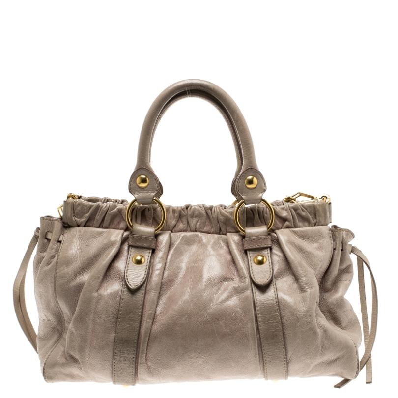 Crafted from glazed leather, this beige Miu Miu bag has a buttoned closure that opens to a spacious fabric lined interior housing a zip pocket. The bag is equipped dual top handles, a detachable shoulder strap, protective metal feet at the bottom