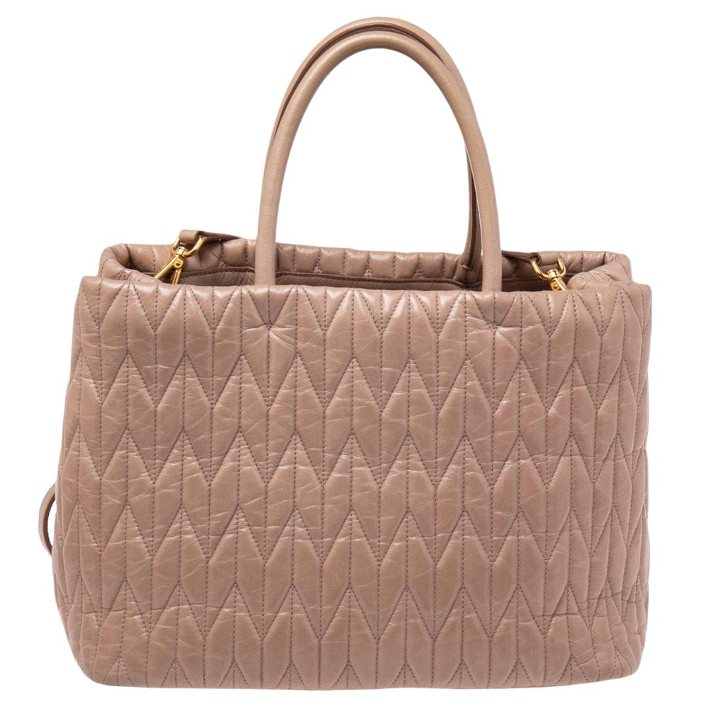 This Miu Miu tote boasts a durable finish and offers style and utmost practicality. Crafted from matelassé leather, it features dual handles, a shoulder strap, and gold-tone hardware. The satin-lined interior has two open compartments and a zipped